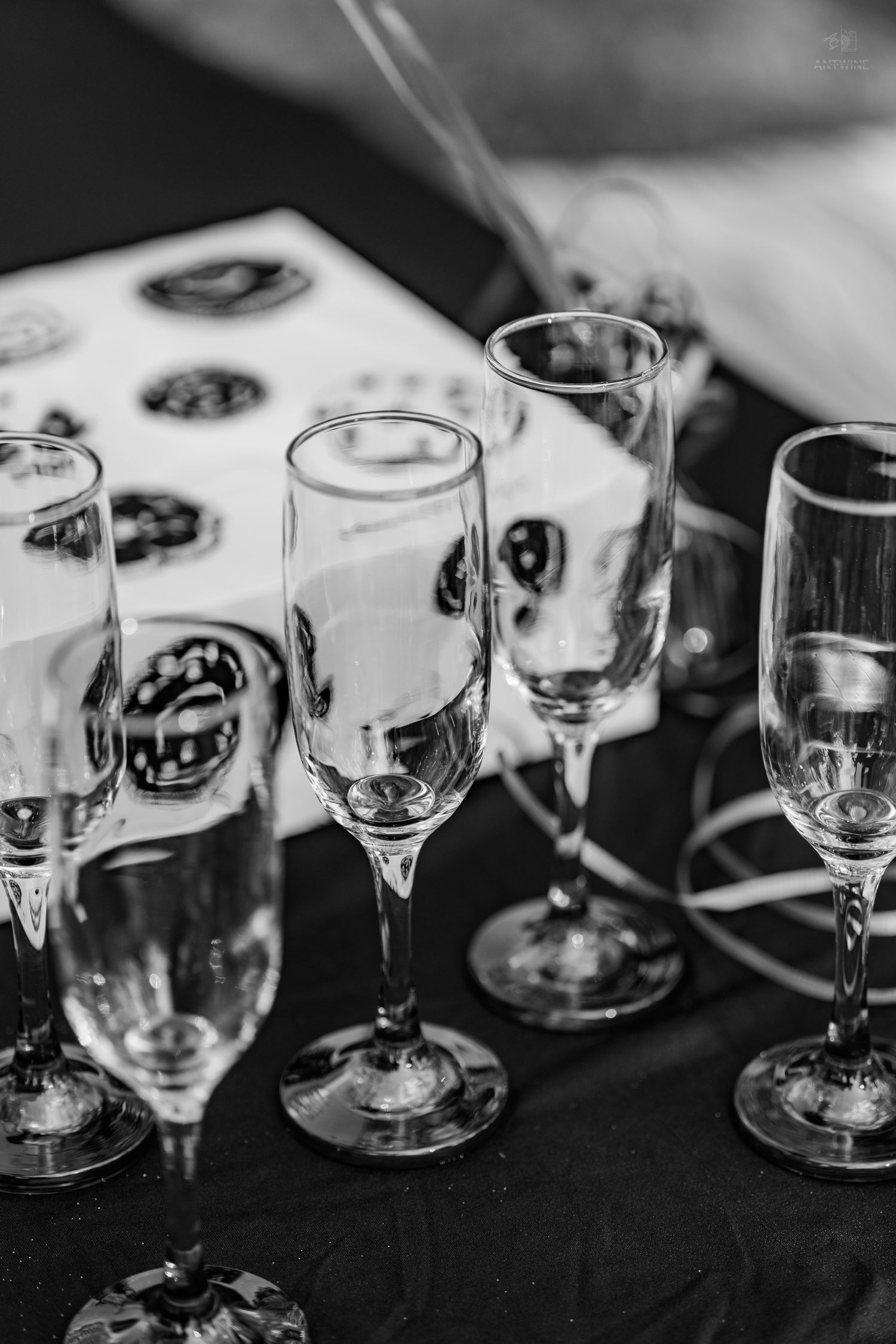 Black and white close-up of multiple empty champagne flutes arranged on a dark surface next to a donut box.
