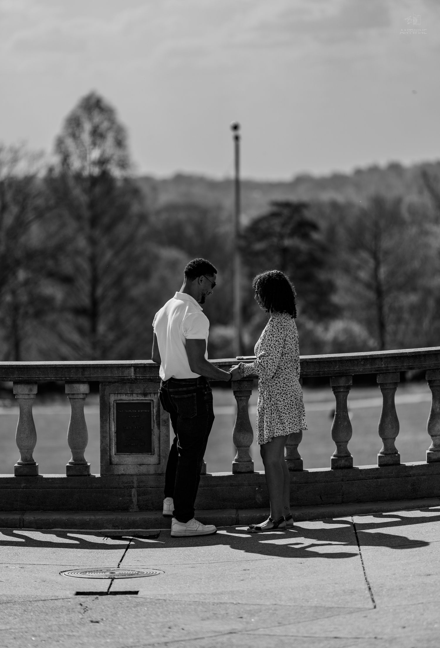 Black and white photo of couple facing each other on sunlit stone terrace in park.