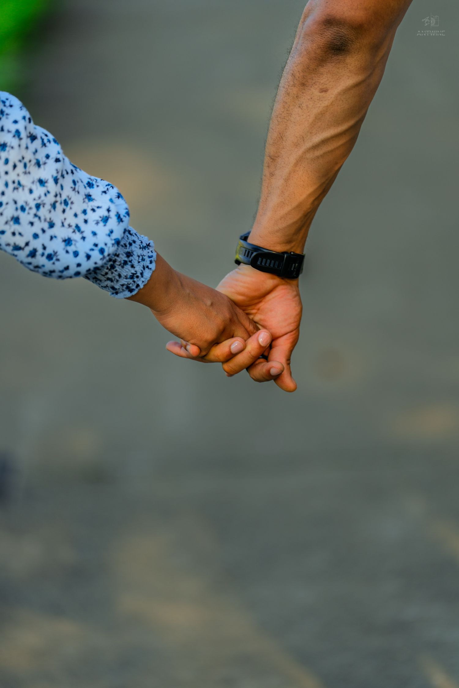Close-up of a couple gently holding hands outdoors, man wearing a black smartwatch on his wrist.