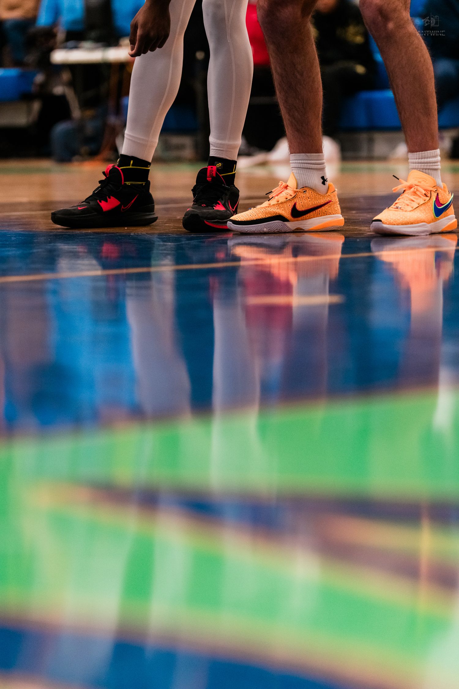 Close-up of basketball players feet in colorful Nike sneakers on a reflective hardwood court.