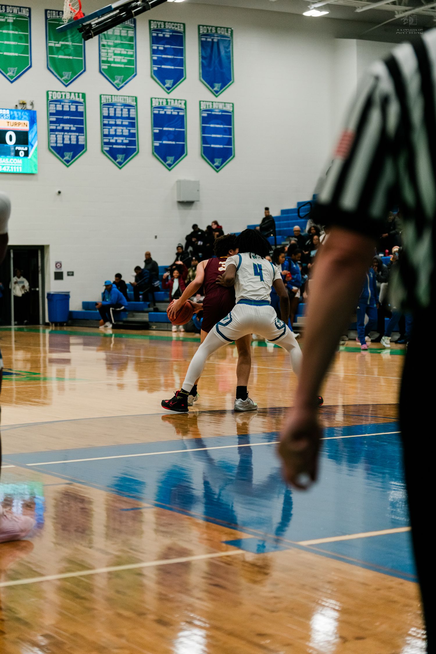 A referee watches closely as two players battle for position during a competitive high school basketball game.