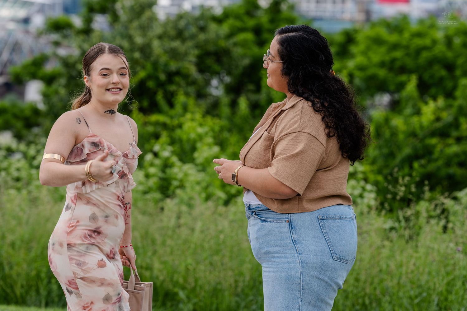 Two women smiling and chatting together in a vibrant green outdoor park.