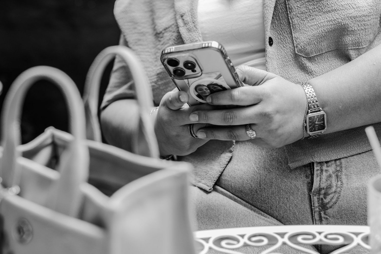 Close-up of woman holding gold iPhone while wearing a bracelet watch, with designer handbag beside her.
