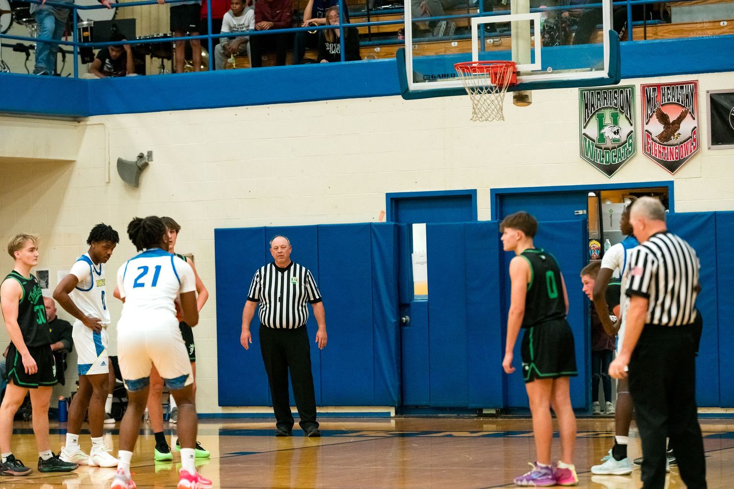 Players and referees stand at the free throw line during a pause in a high school basketball game.