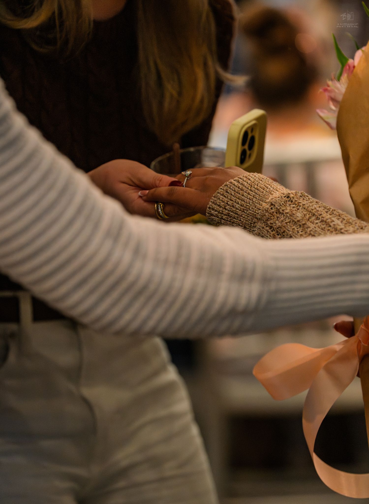 Close-up of two women examining a ring while holding flowers with a pink ribbon at a celebration.