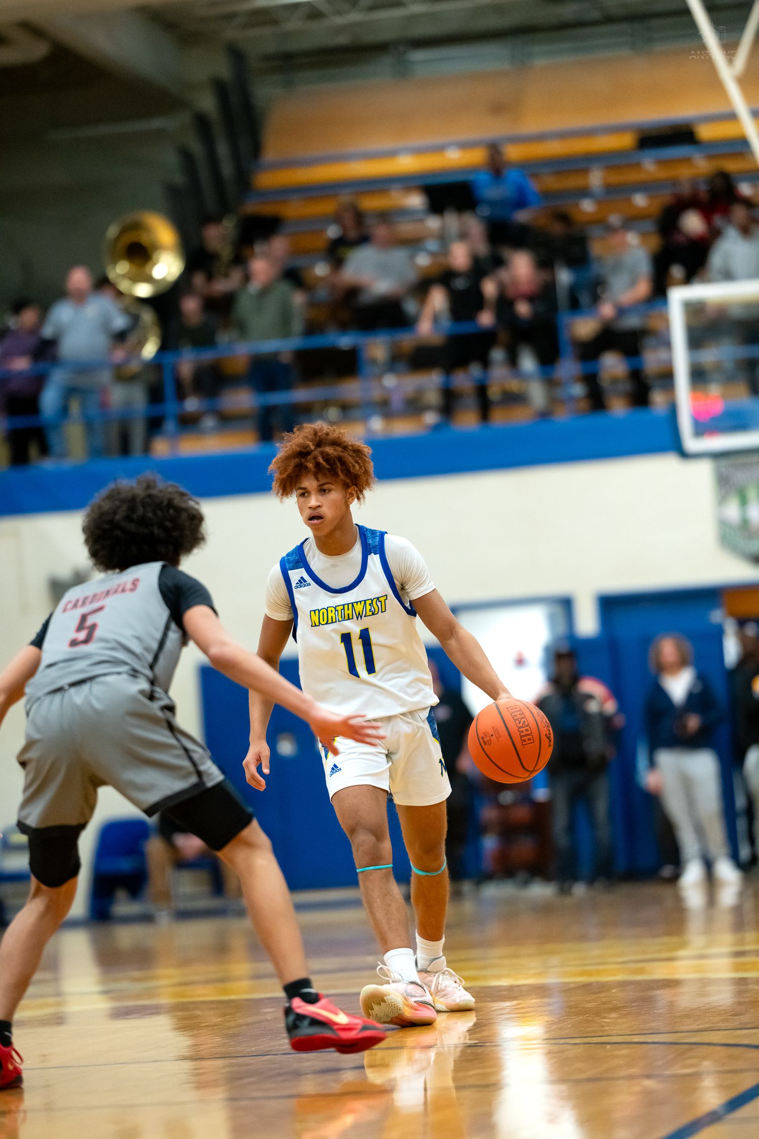 High school basketball player #11 dribbles past defender #5 in packed gymnasium.