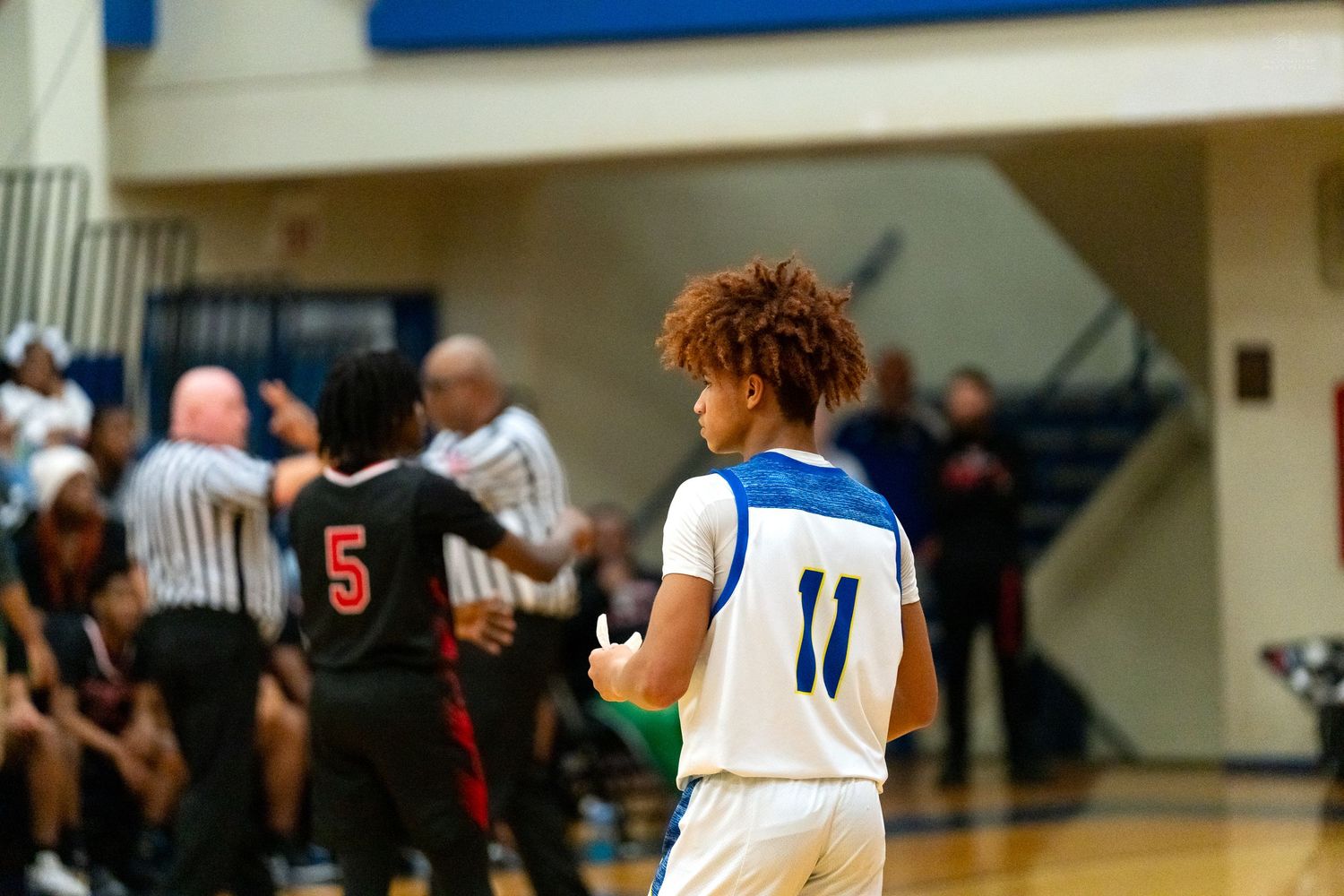 High school basketball player wearing number 11 blue jersey stands on court during a competitive game.