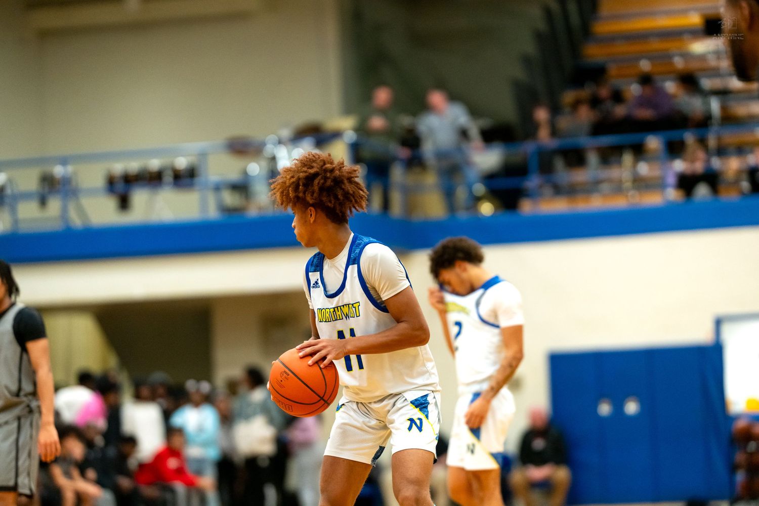 High school basketball player #11 handles the ball during indoor game with teammates visible in background.