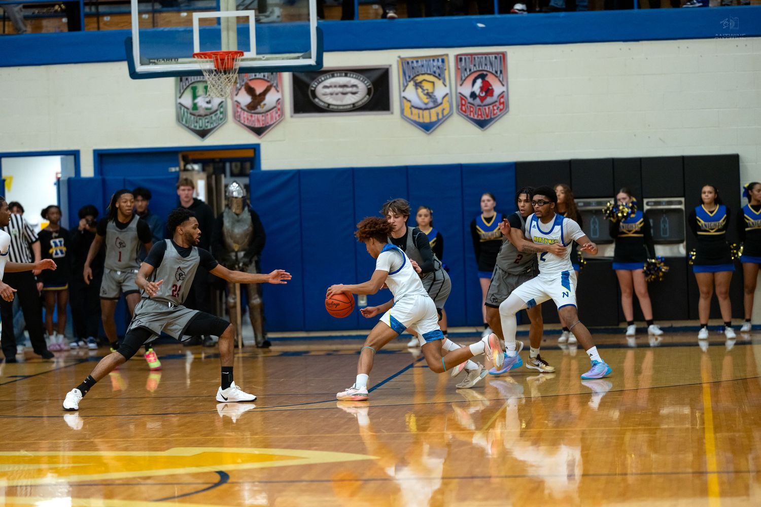 High school basketball players in blue and white uniforms dribble during fast-paced indoor game.