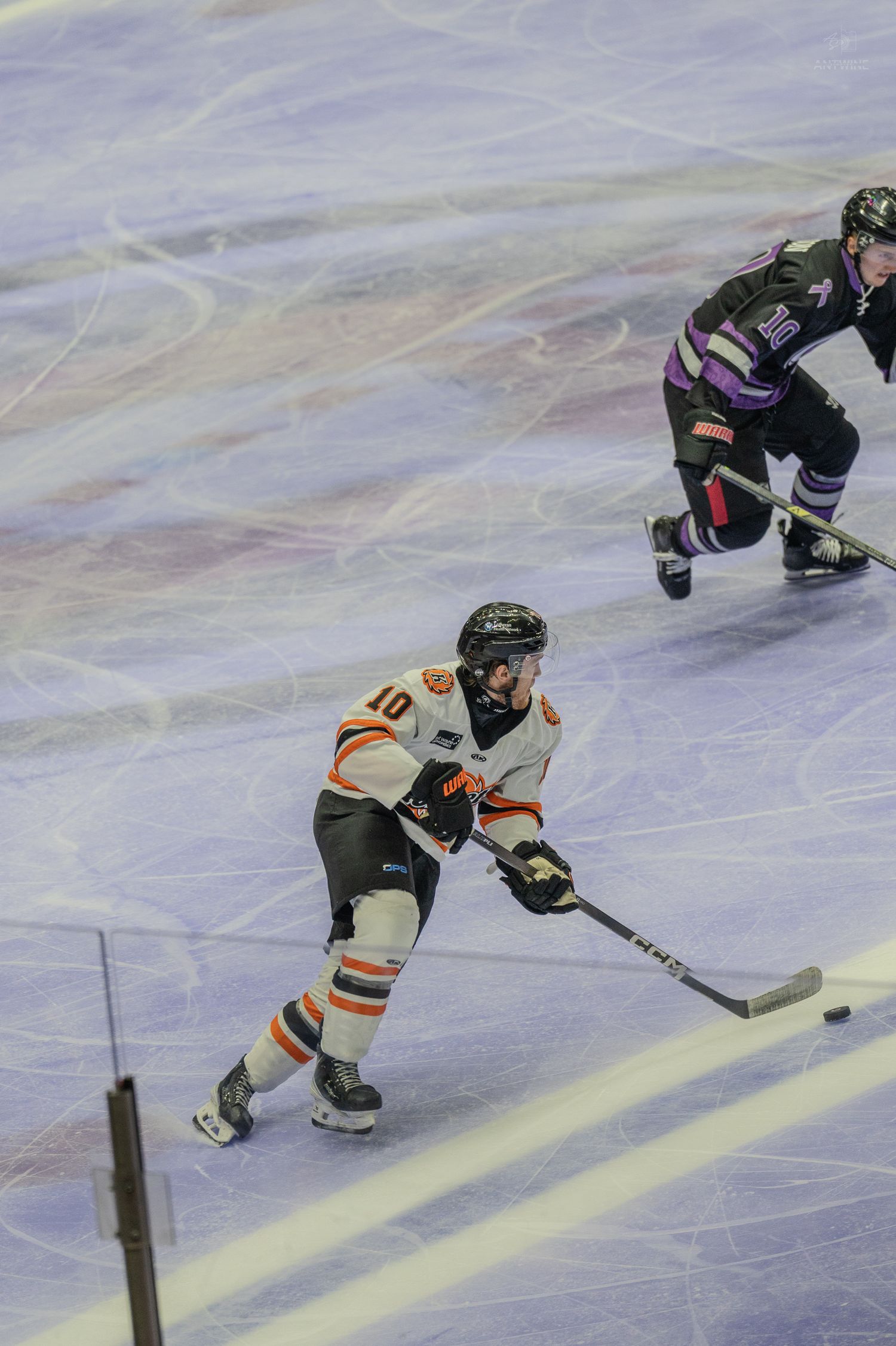 Hockey player number 10 in white and orange uniform handles the puck on ice during a competitive game.