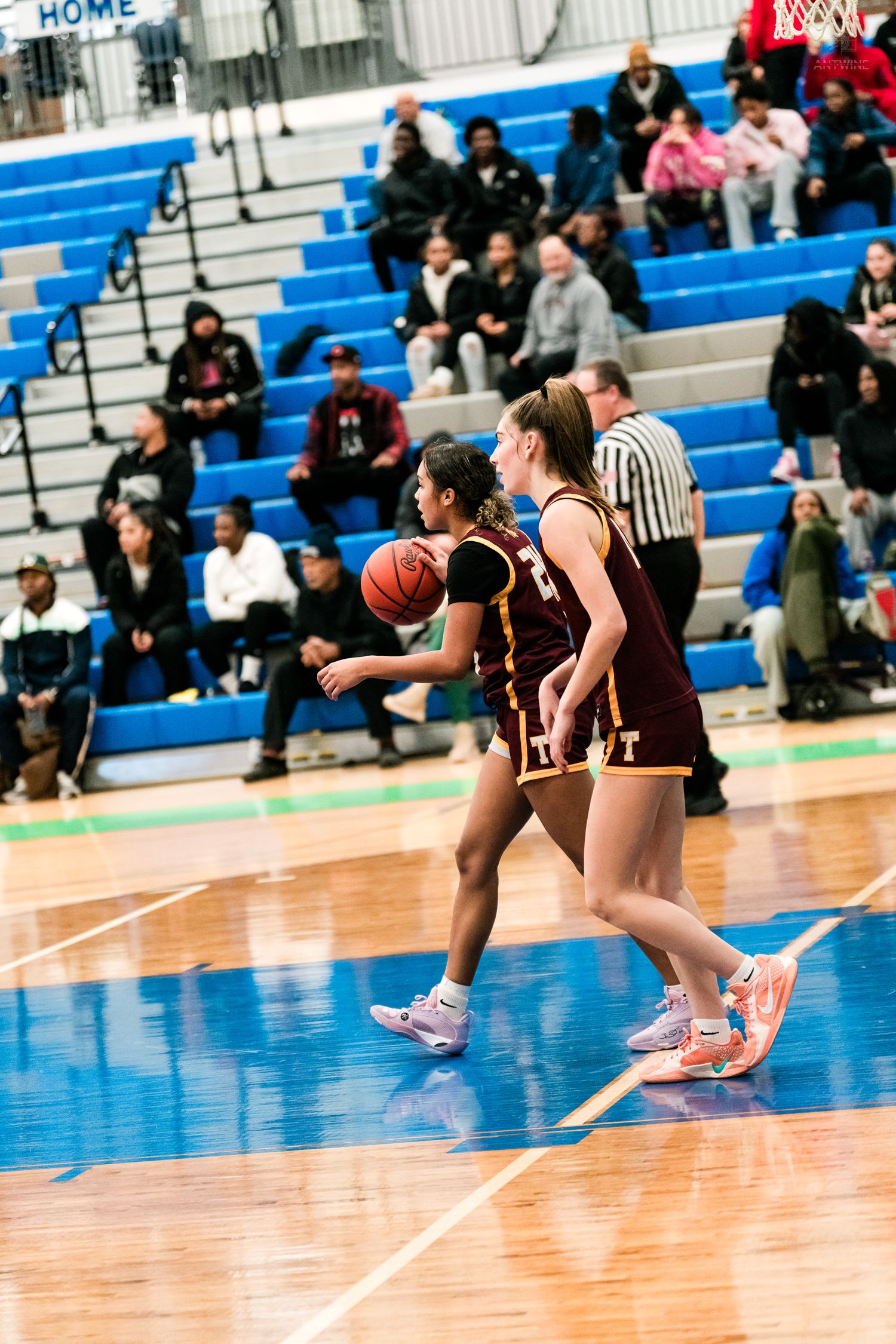 Two Turpin female basketball players in maroon dribble upcourt together during an indoor high school basketball game.