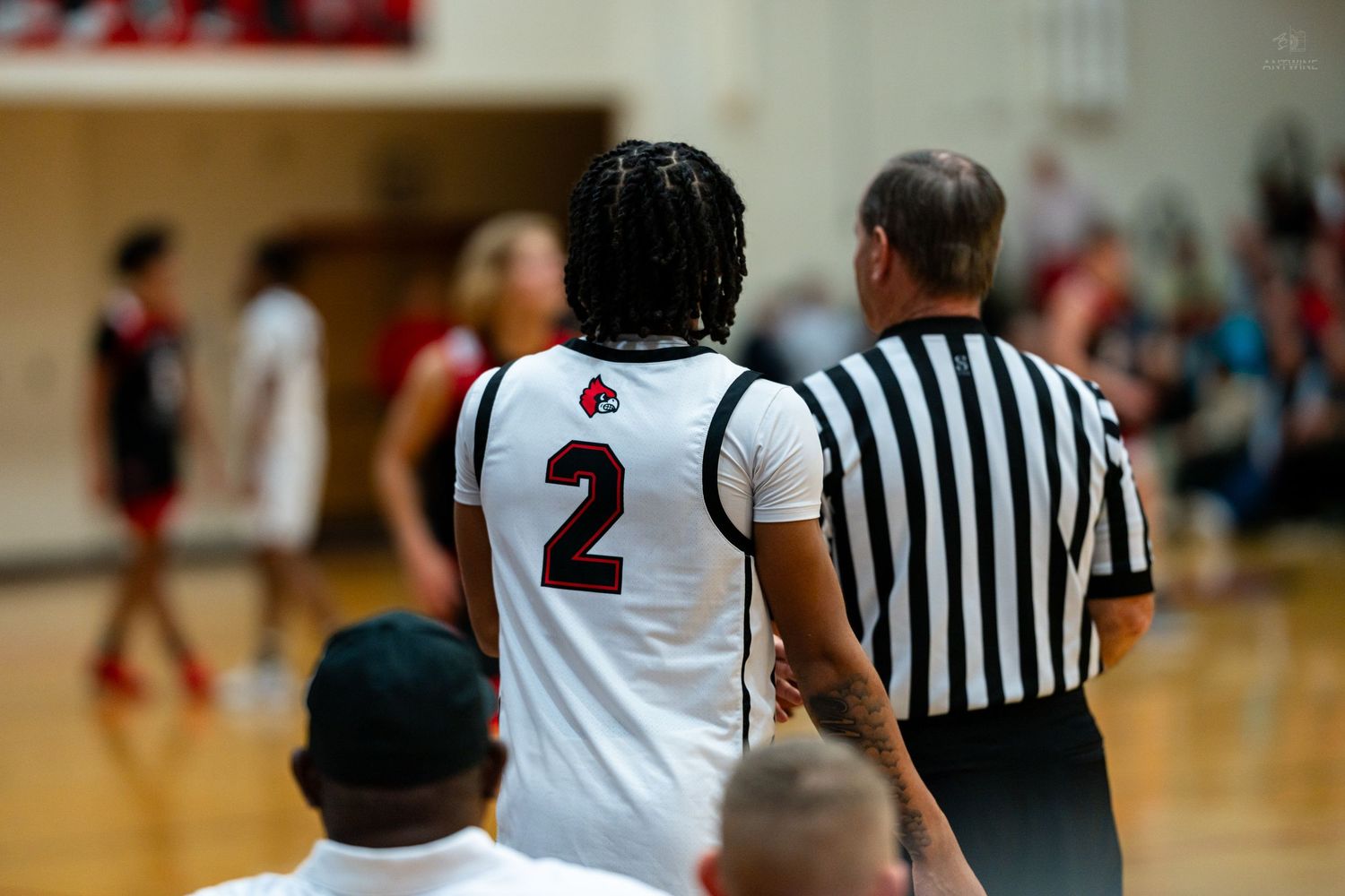Basketball player wearing number 2 jersey stands near referee during high school game.