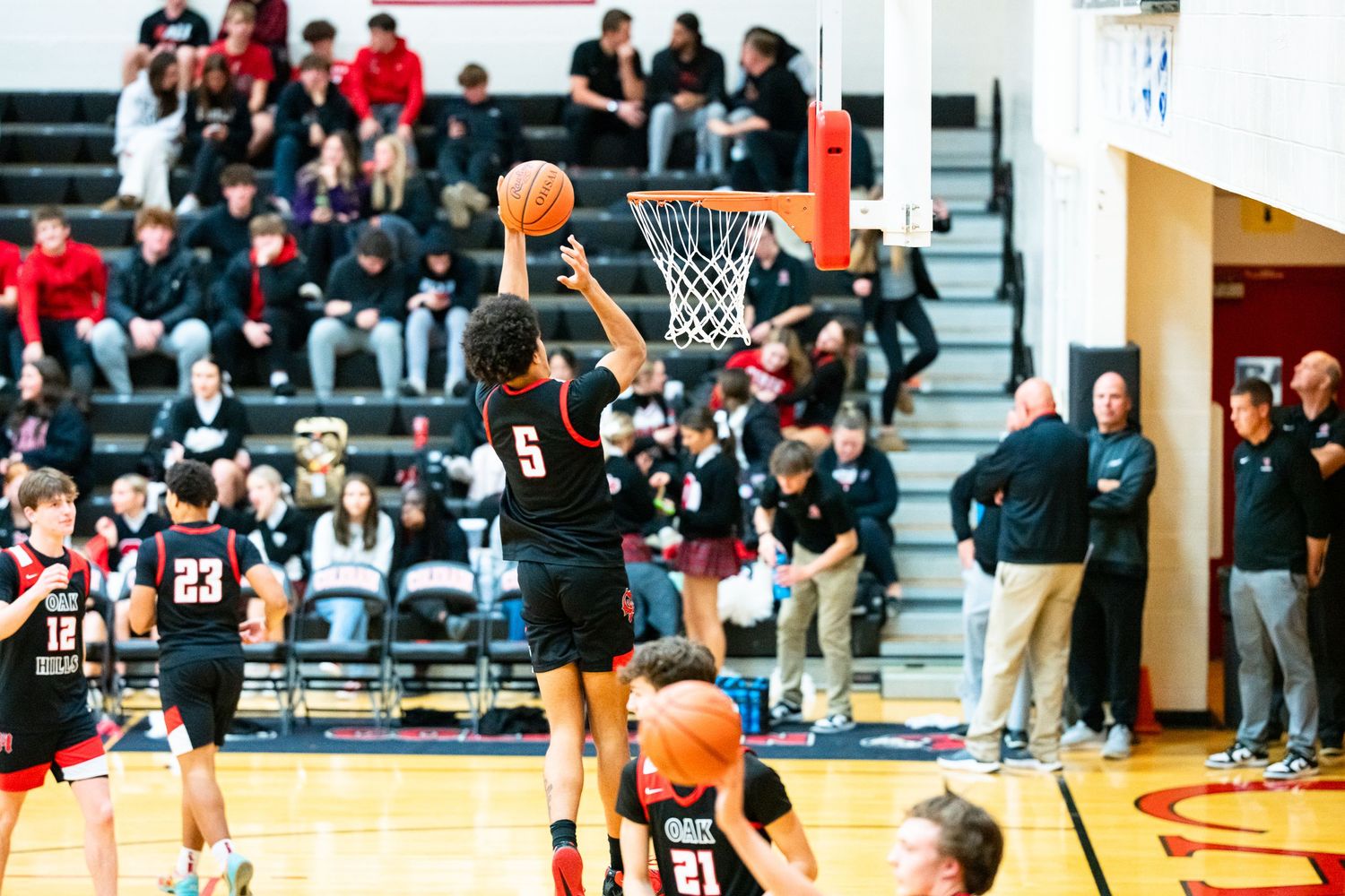 High school basketball player number 5 shoots near the basket during a game with fans in the stands.