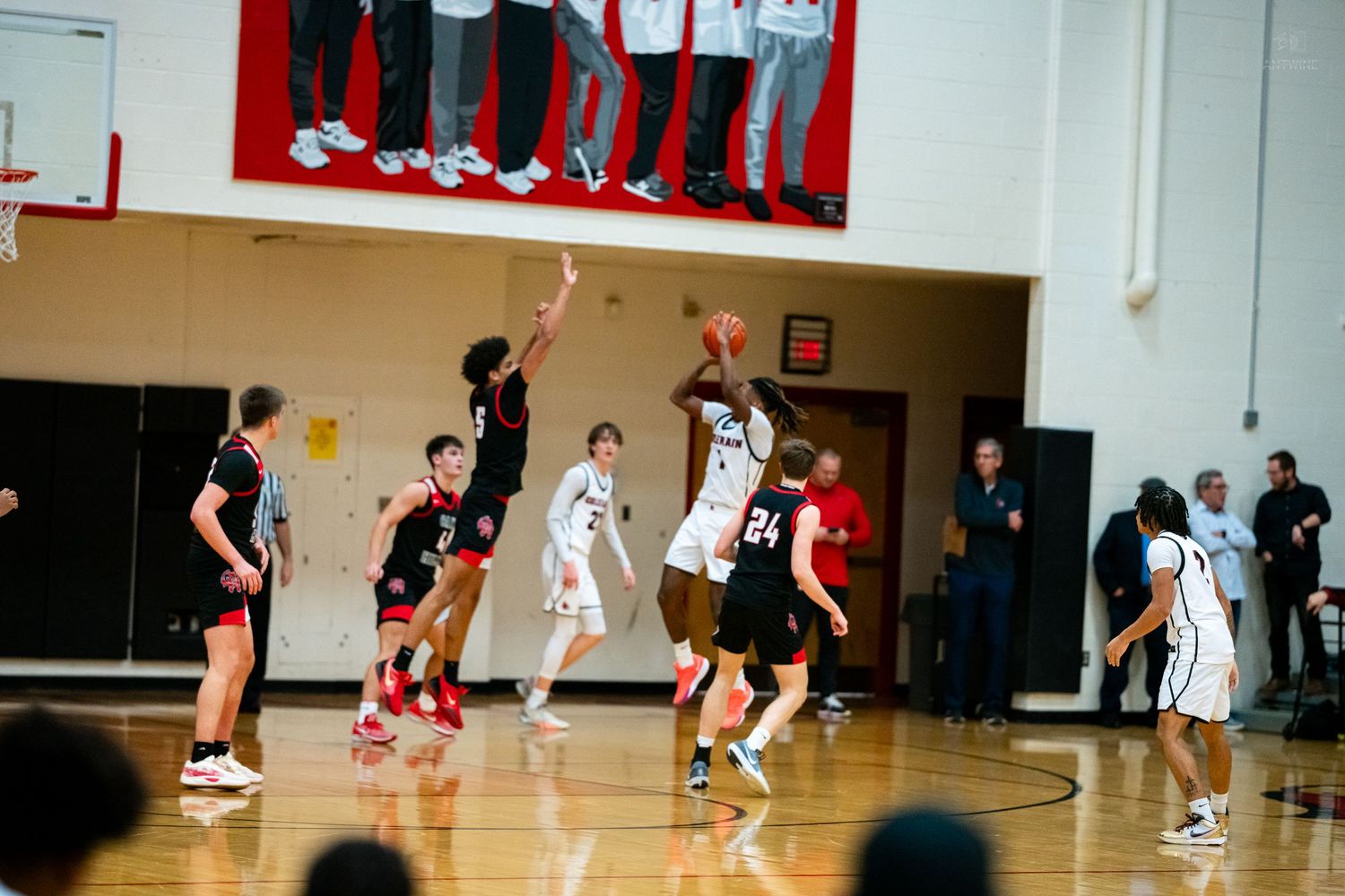 High school basketball player attempts jump shot while defenders contest during an indoor gymnasium game.