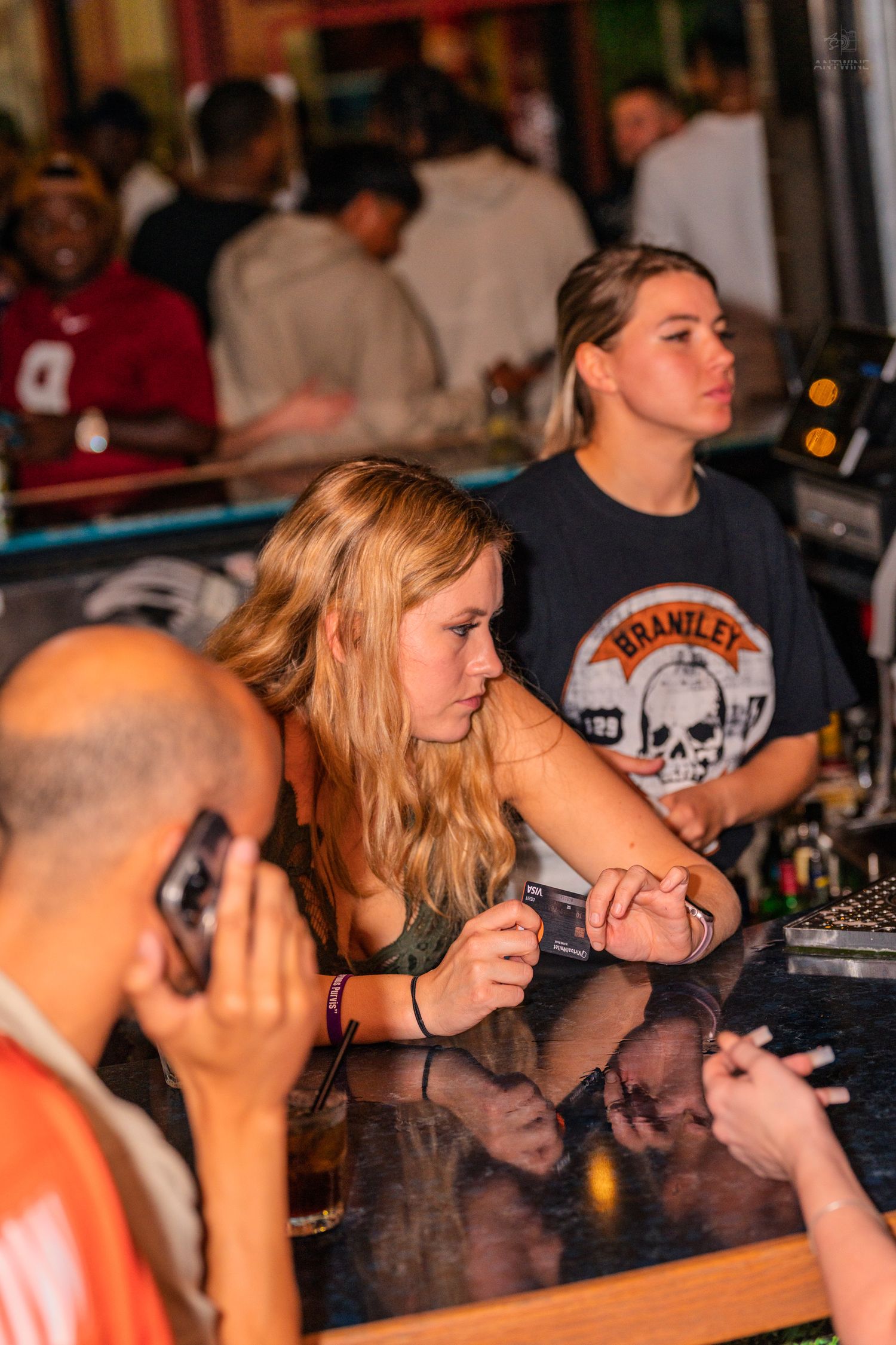 Two blonde women waiting at a bar counter during a busy nightclub event.