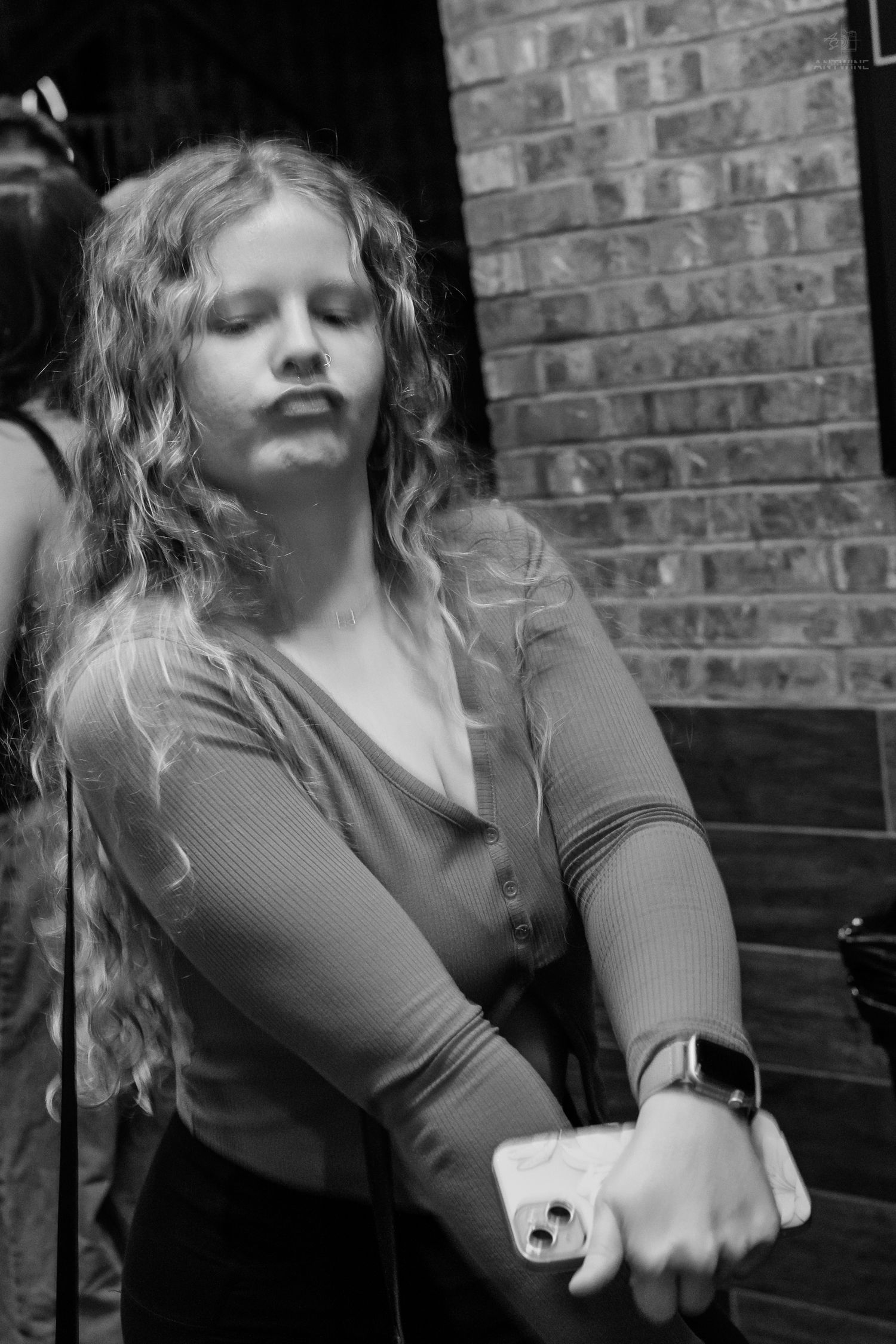 A young curly-haired woman with eyes closed holds her phone outside a brick building.