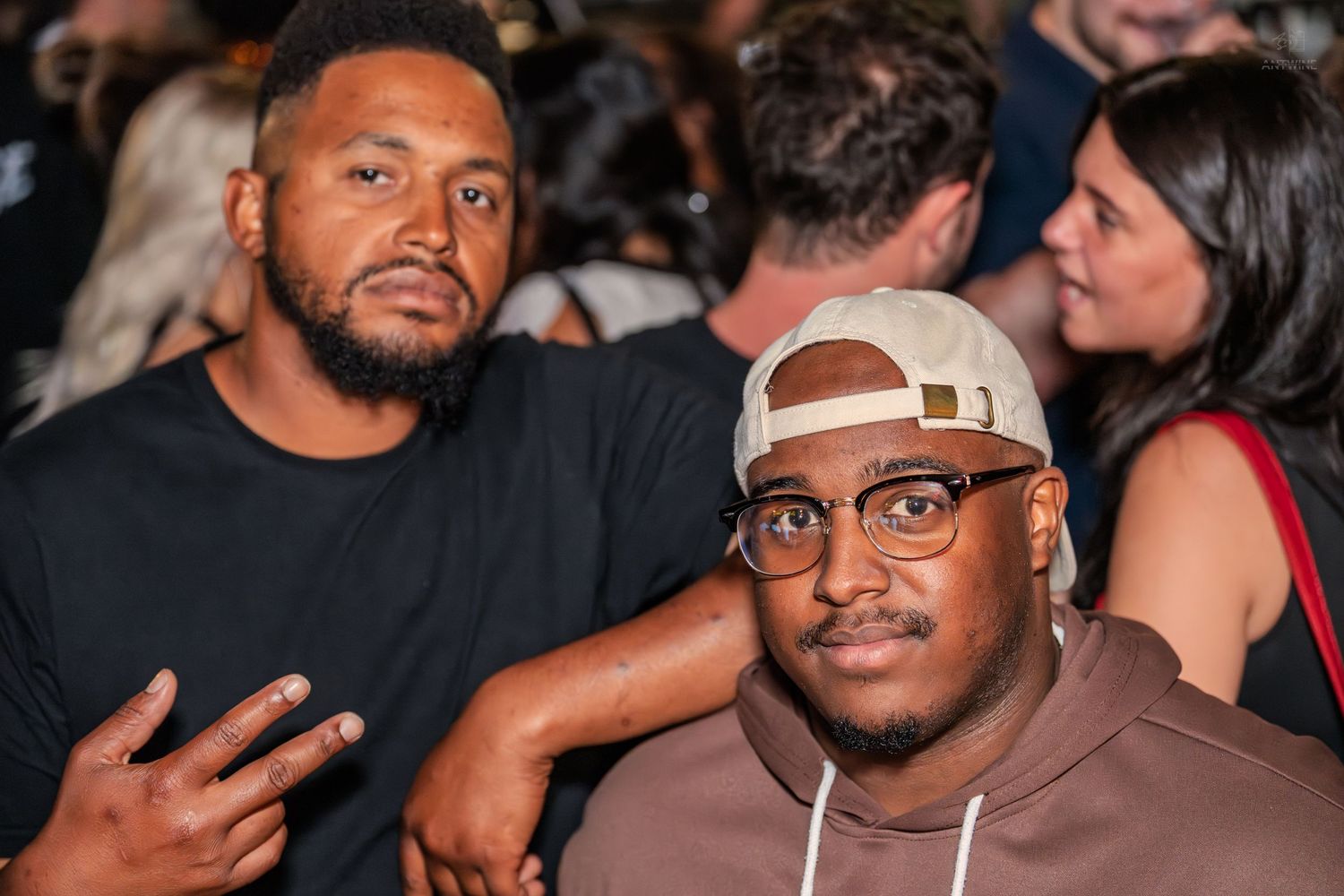 Two men posing together at a lively indoor social event.