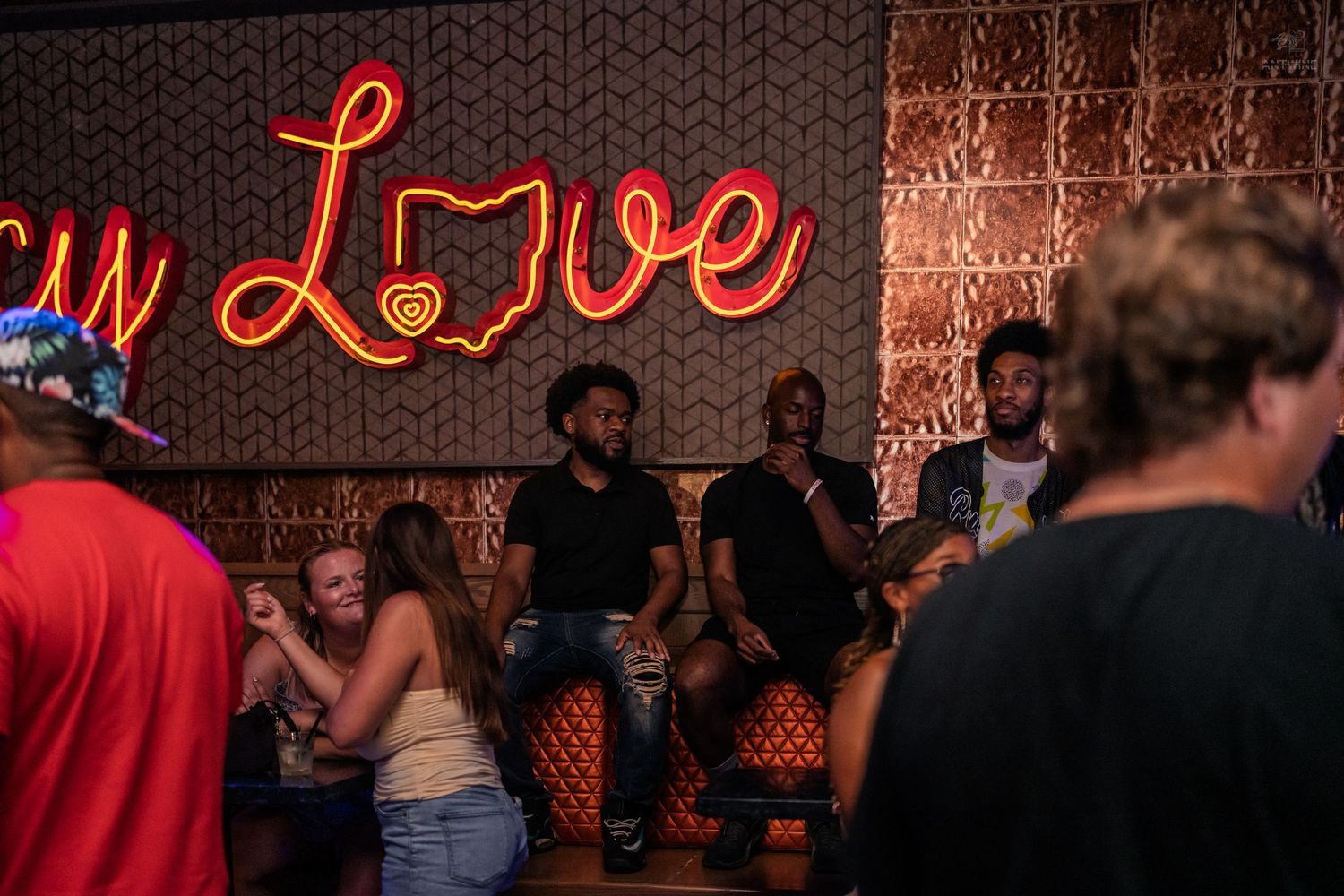 Group of friends relaxing near a glowing neon Love sign in a trendy bar.