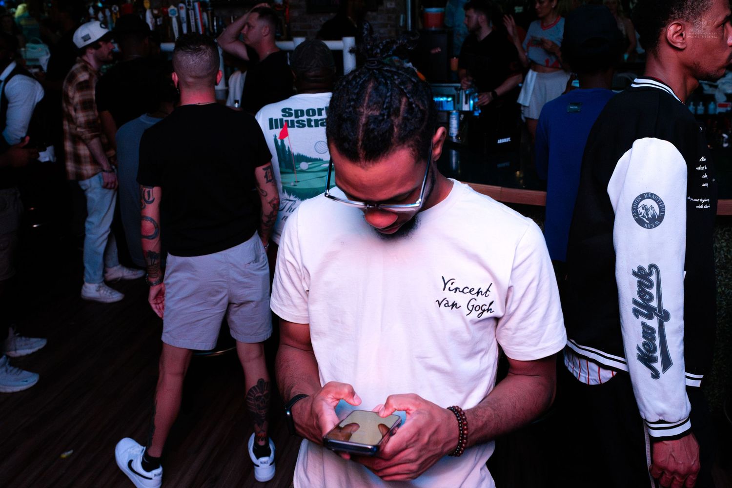 Man in Vincent Van Gogh shirt looking at phone on outdoor deck at a party.