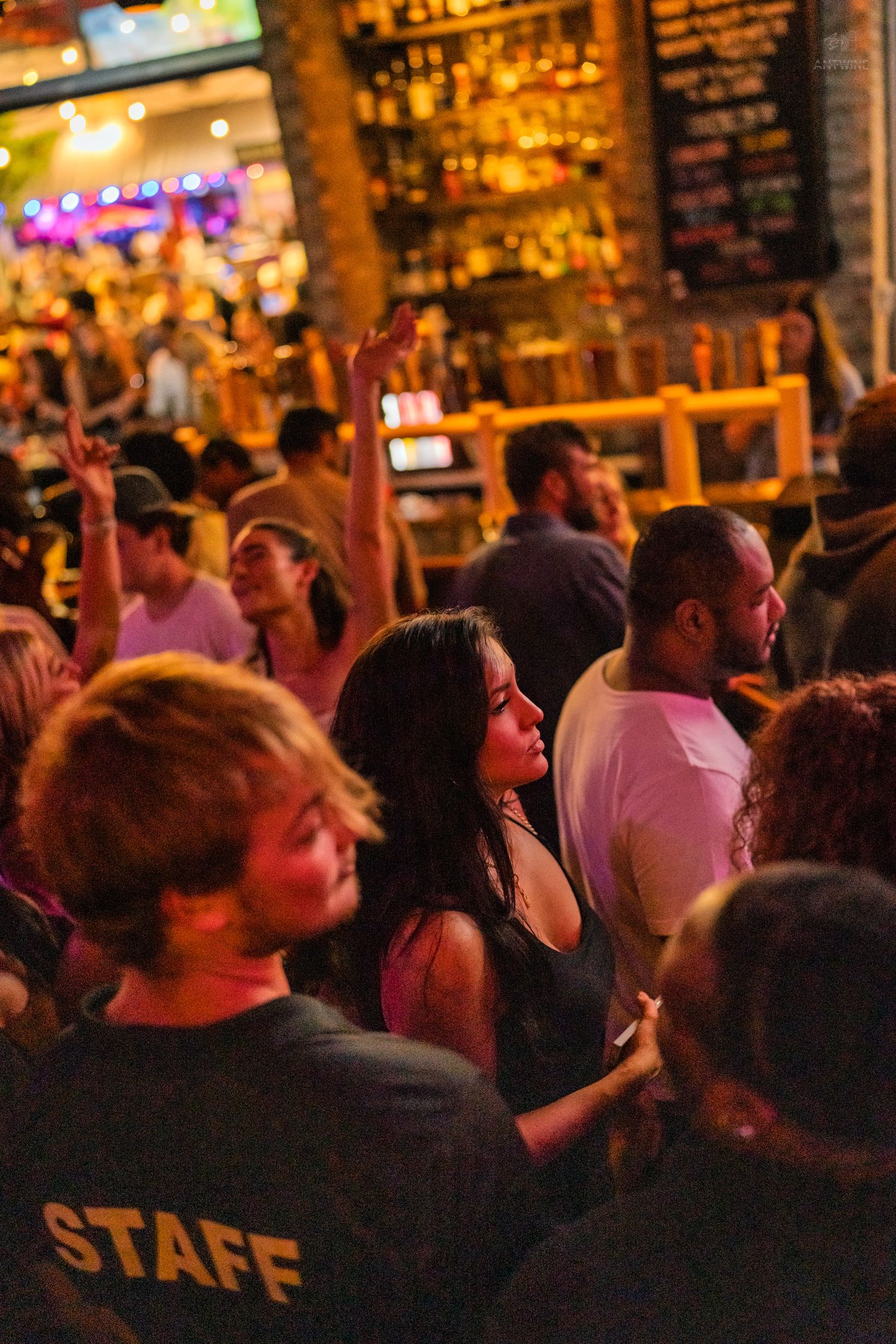 Diverse crowd dancing and socializing at a warmly lit bar venue.