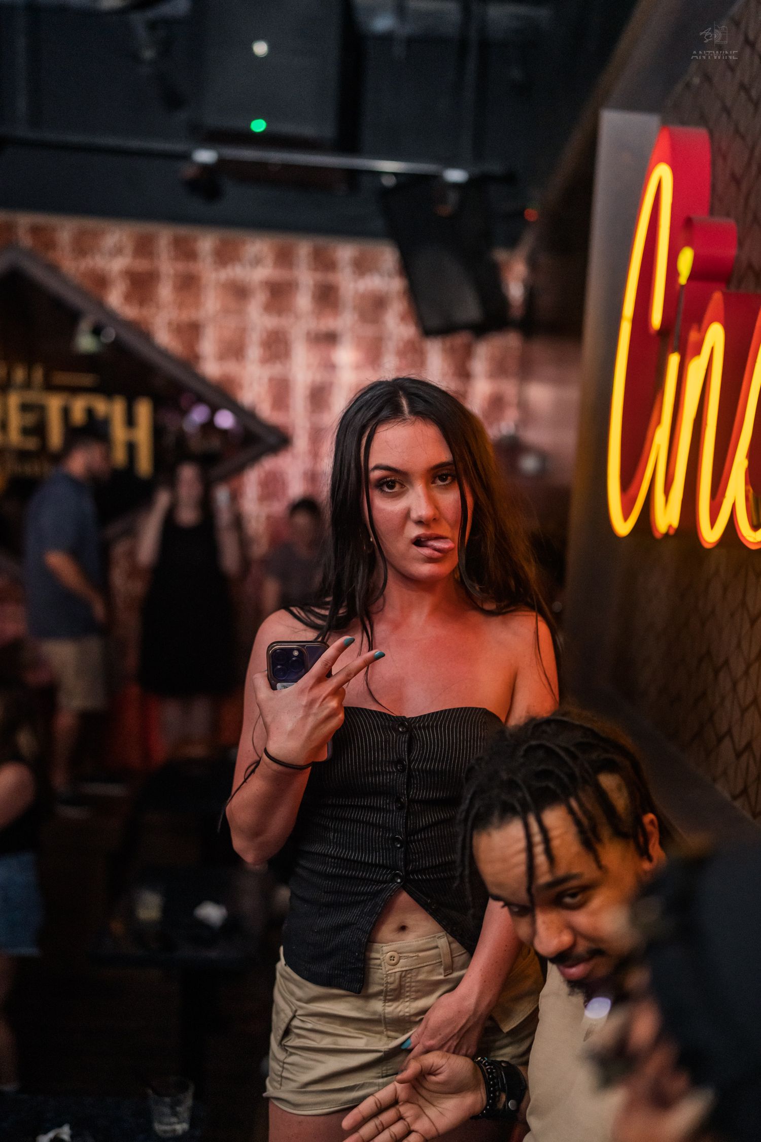 Brunette woman holding phone near glowing Cincy neon sign at a nightclub event.