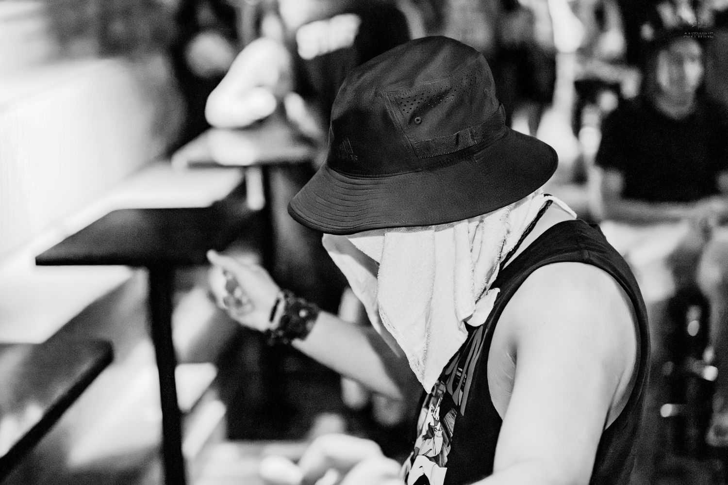Black and white photo of person in bucket hat looking down at outdoor event.