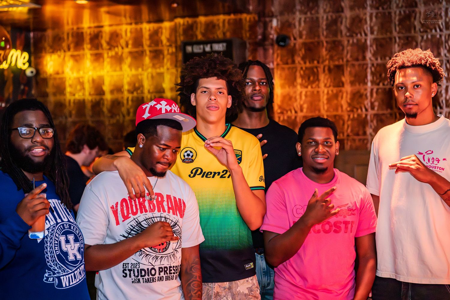 Group of young men posing together at a vibrant nightclub event with colorful lighting.