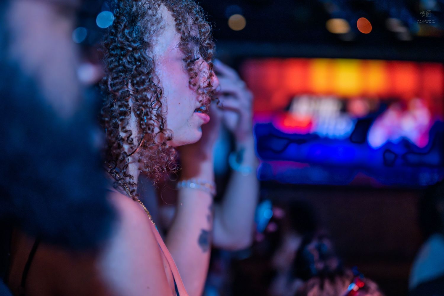 Woman with curly hair in profile view at dimly lit nightclub with neon lights.