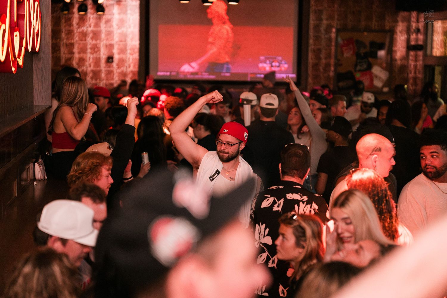 Energetic crowd dancing at a packed nightclub with a screen in the background.
