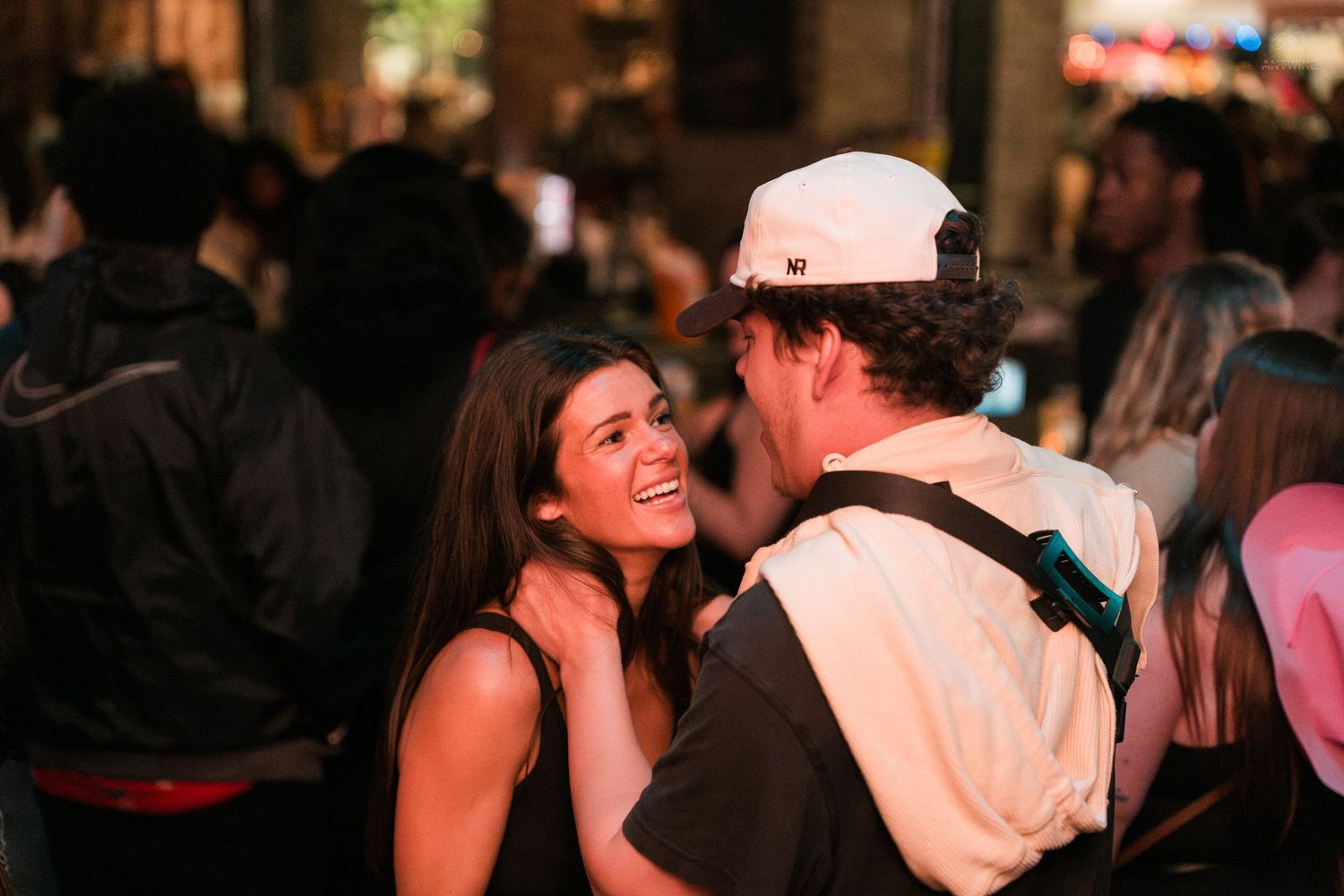 Young couple smiling and sharing a moment together at a lively outdoor nighttime event or bar.