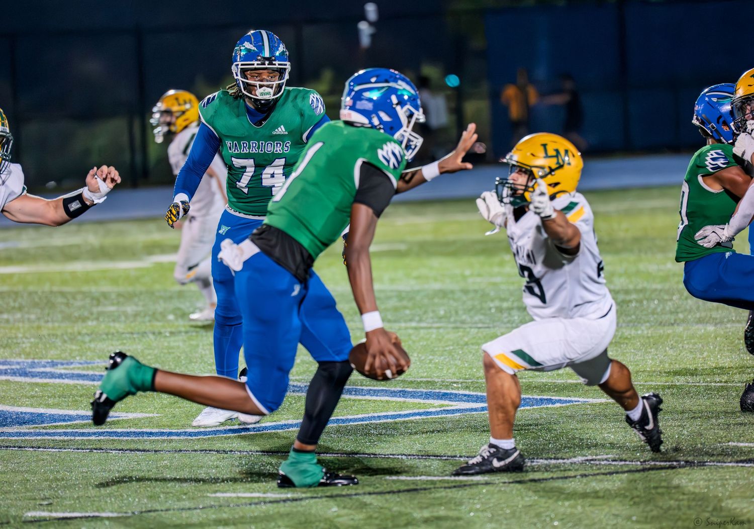 High school football quarterback in green jersey scrambles away from defenders during a night game.