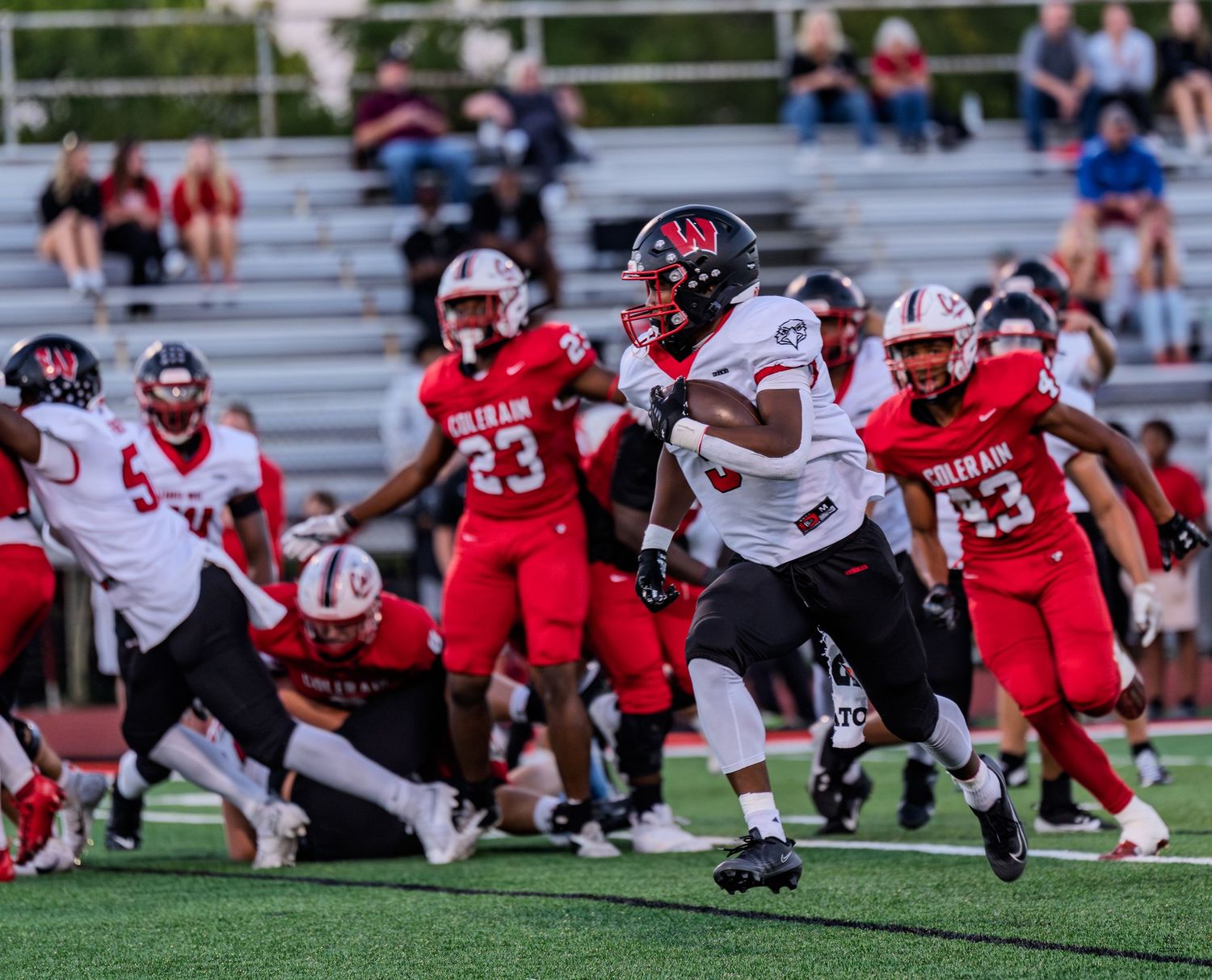 Running back in white uniform breaks through Colerain Cardinals defense during high school football game.