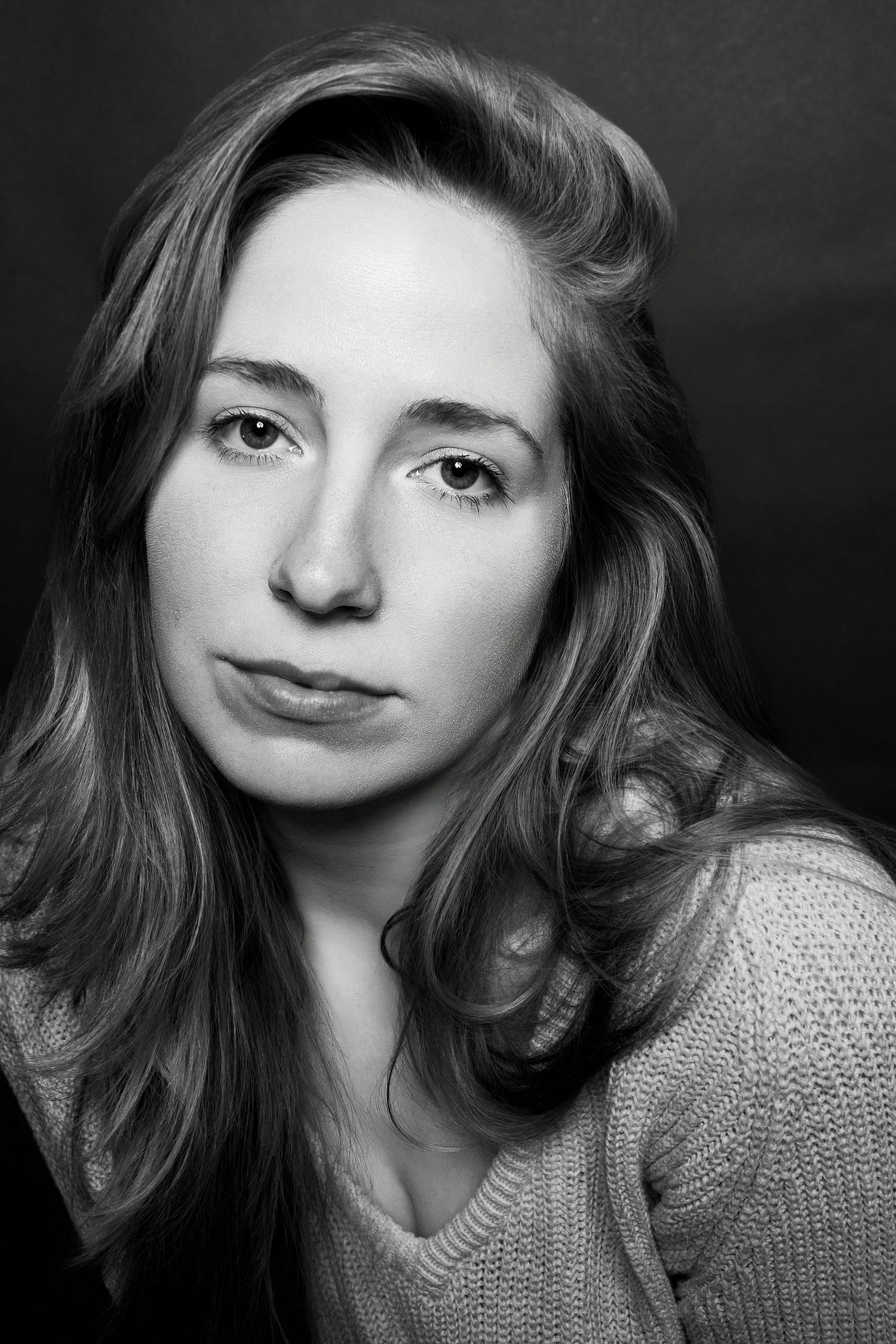 Black and white close-up studio portrait of a young woman with long hair in a knit sweater.