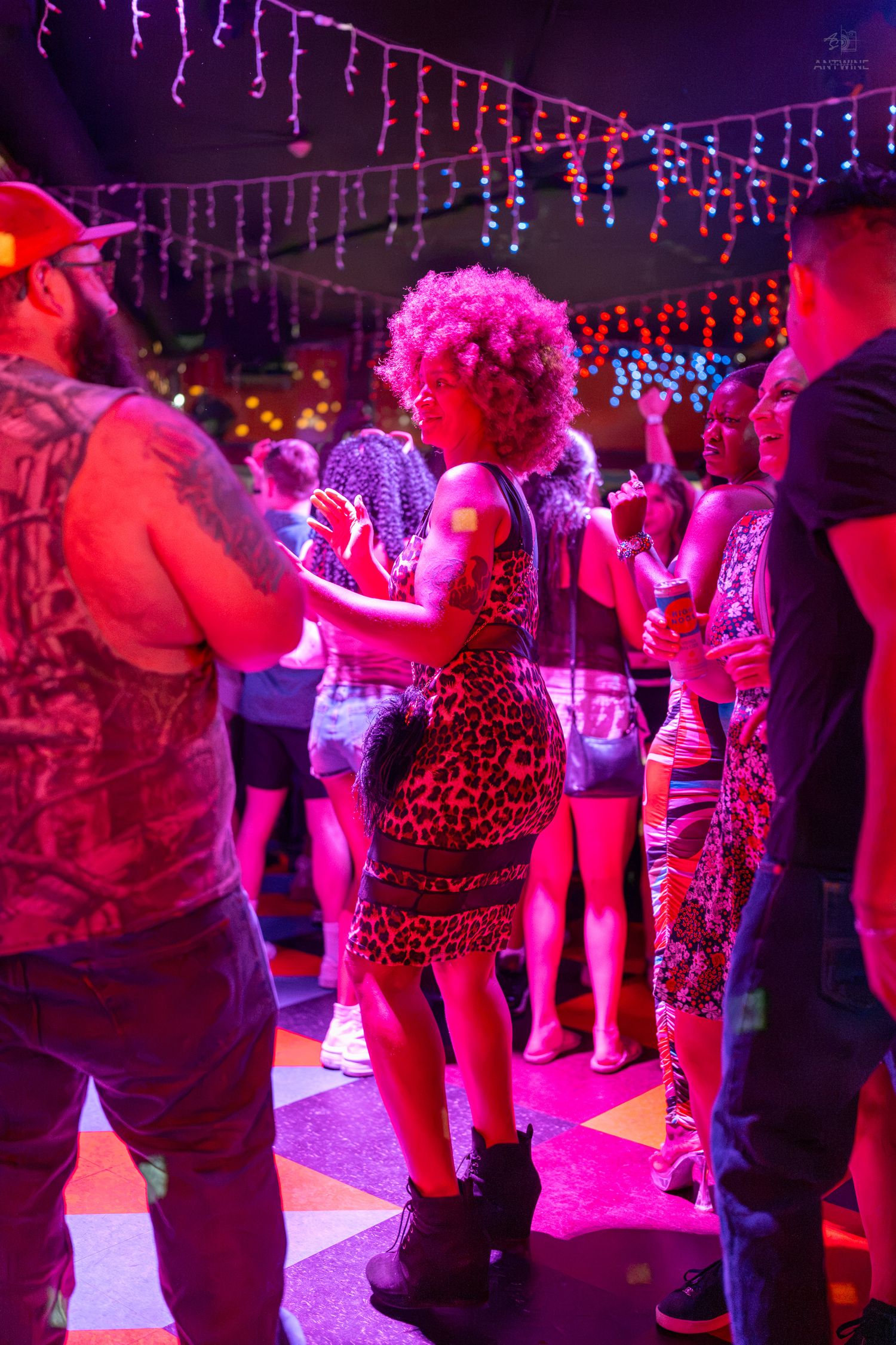 Woman in leopard dress dancing under colorful lights at a lively nightclub party with other guests.