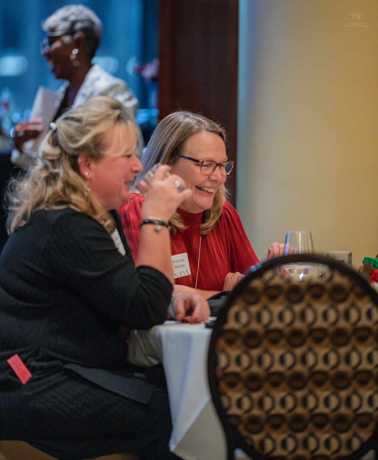 Two women laugh together at a banquet table during a professional networking event.
