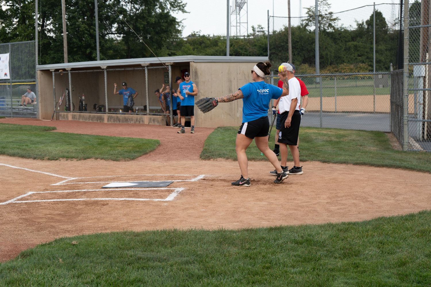 Players compete in a softball game at an outdoor diamond, with a batter and coach near home plate.