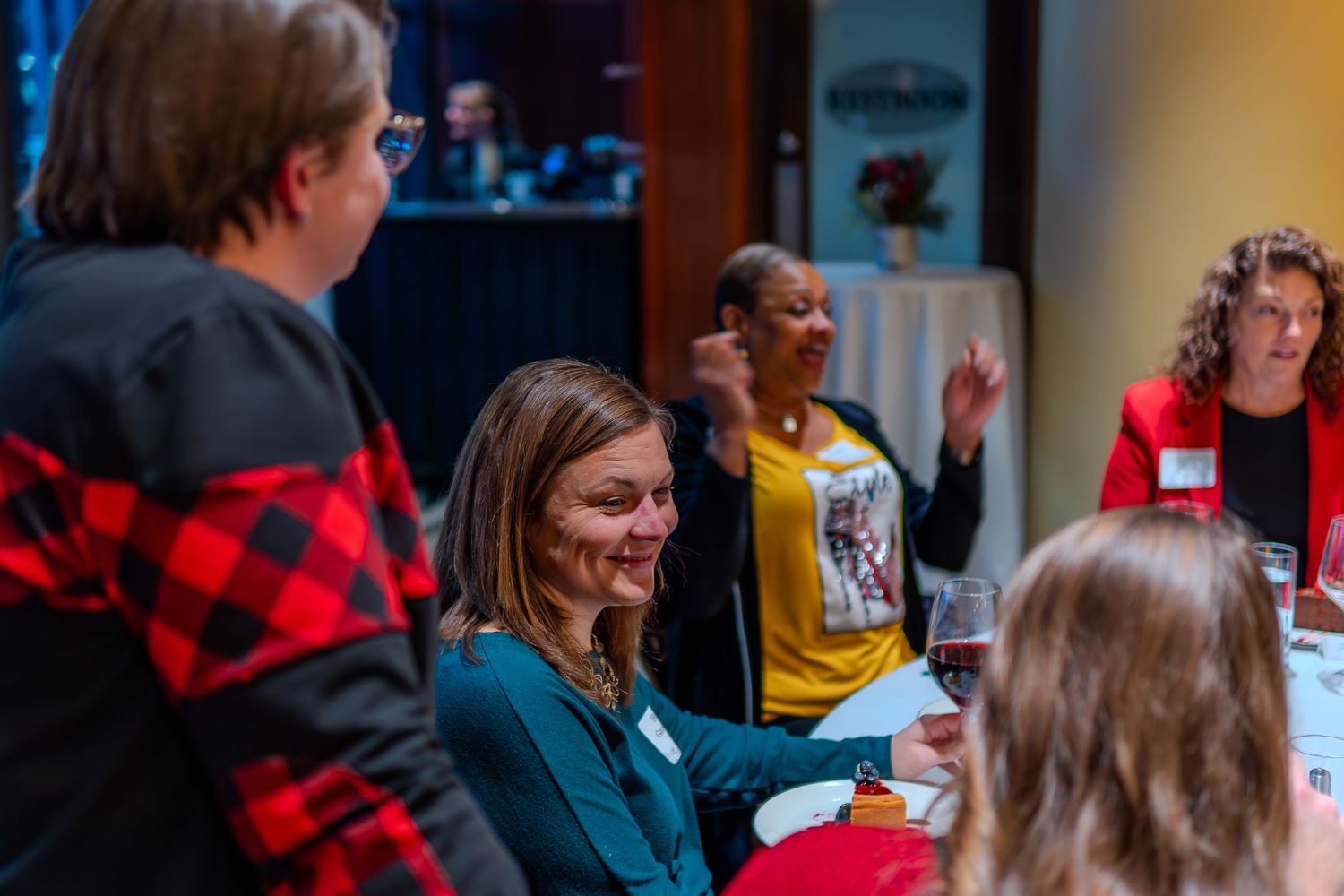 Smiling women networking at an indoor professional event, engaged in lively conversation around a table.