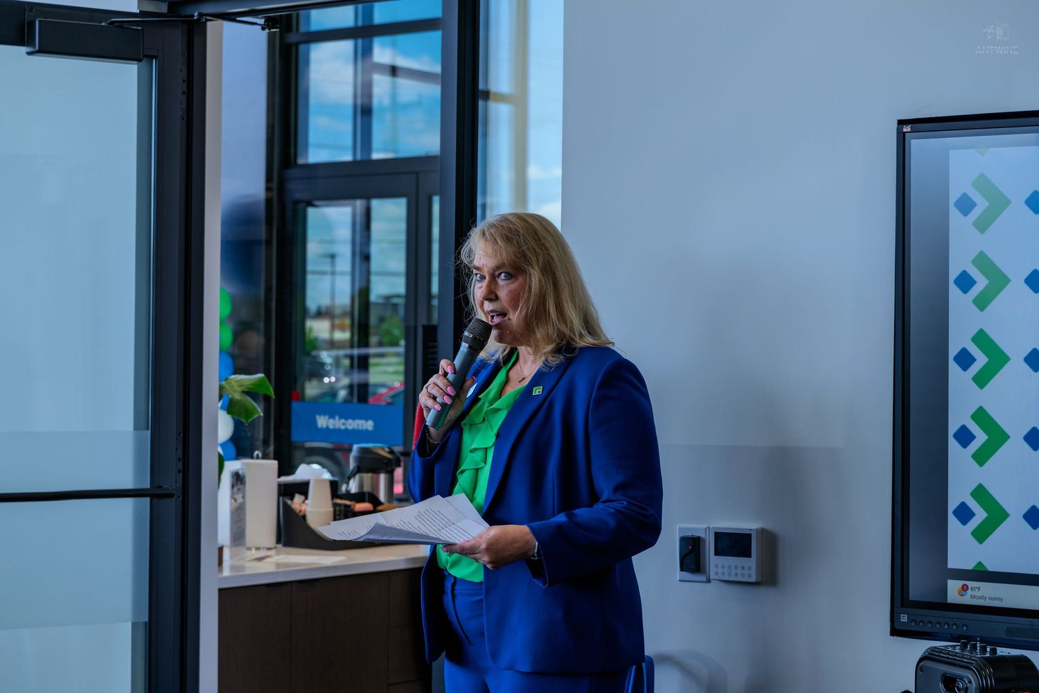 Woman in blue blazer speaking at podium with microphone at a corporate welcome event.