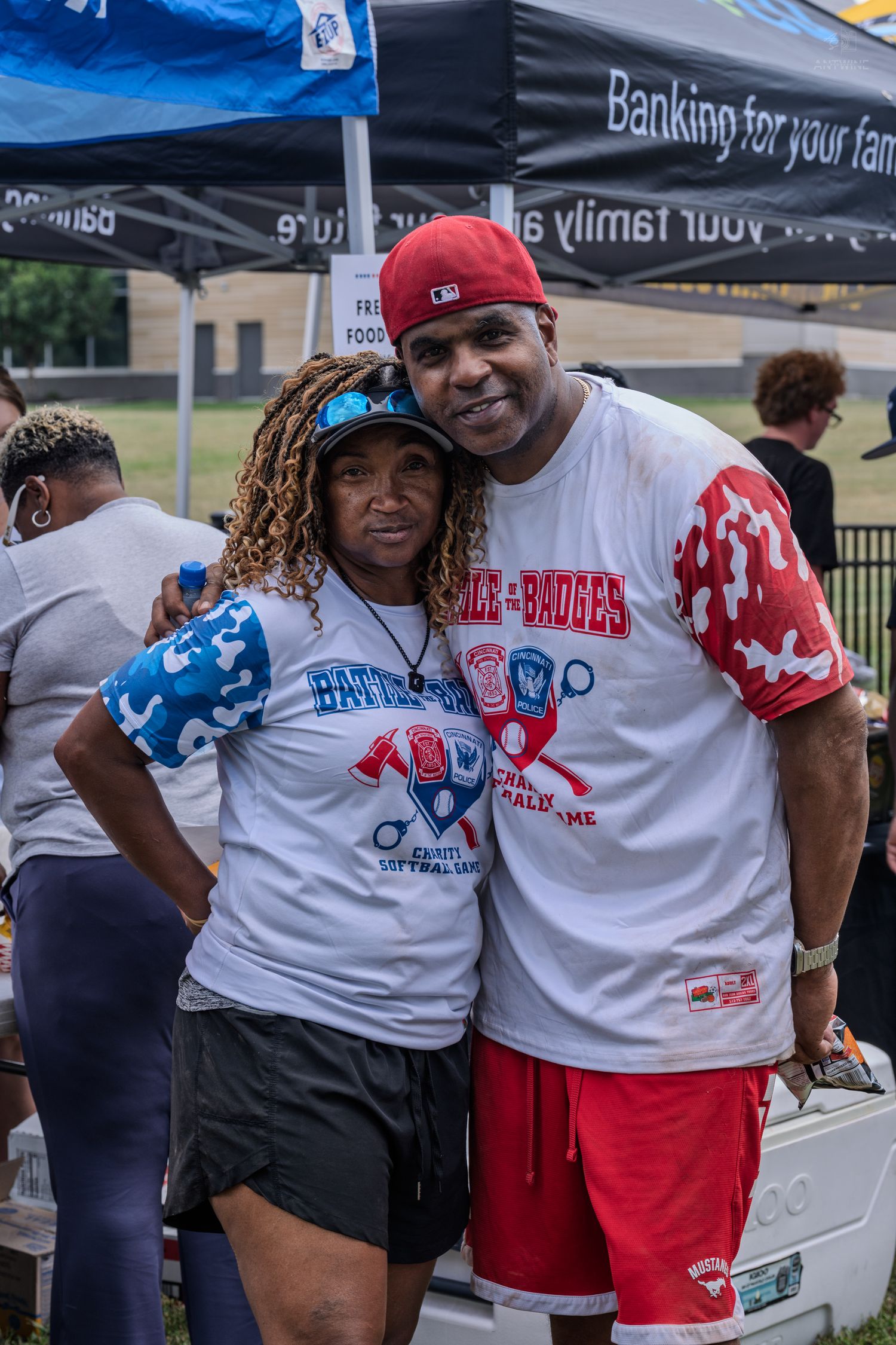 Couple posing in Battle of the Badges charity softball game shirts at outdoor event.
