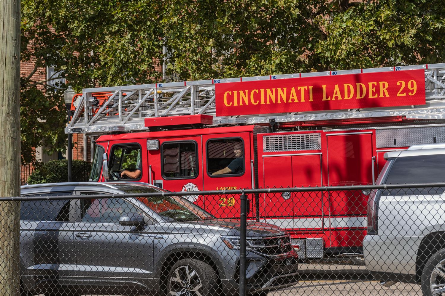 Cincinnati Ladder 29 red fire truck parked behind chain-link fence in urban parking lot.