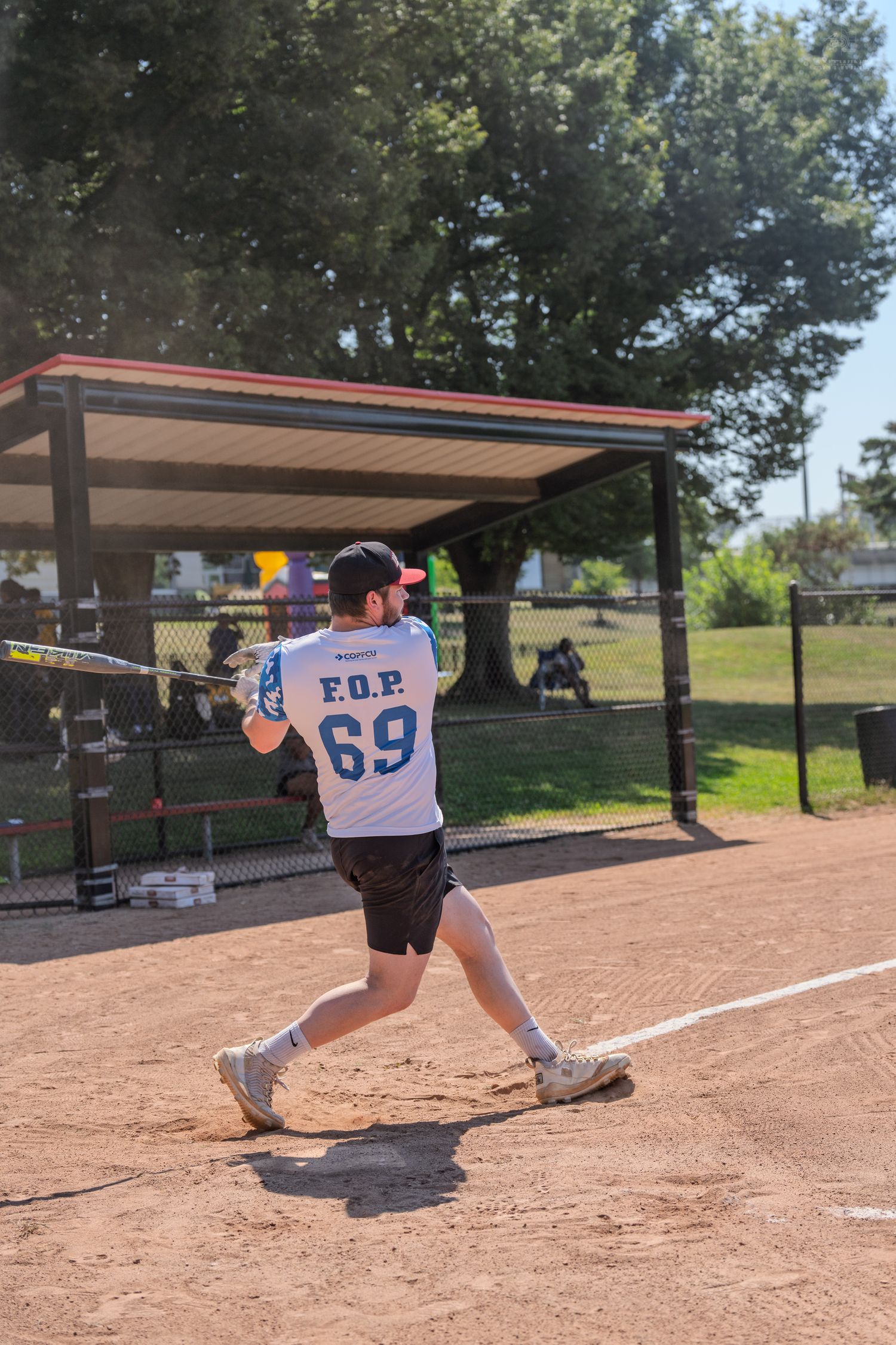 Softball batter in F.O.P. 69 jersey swinging at ball during outdoor game on sunny afternoon.