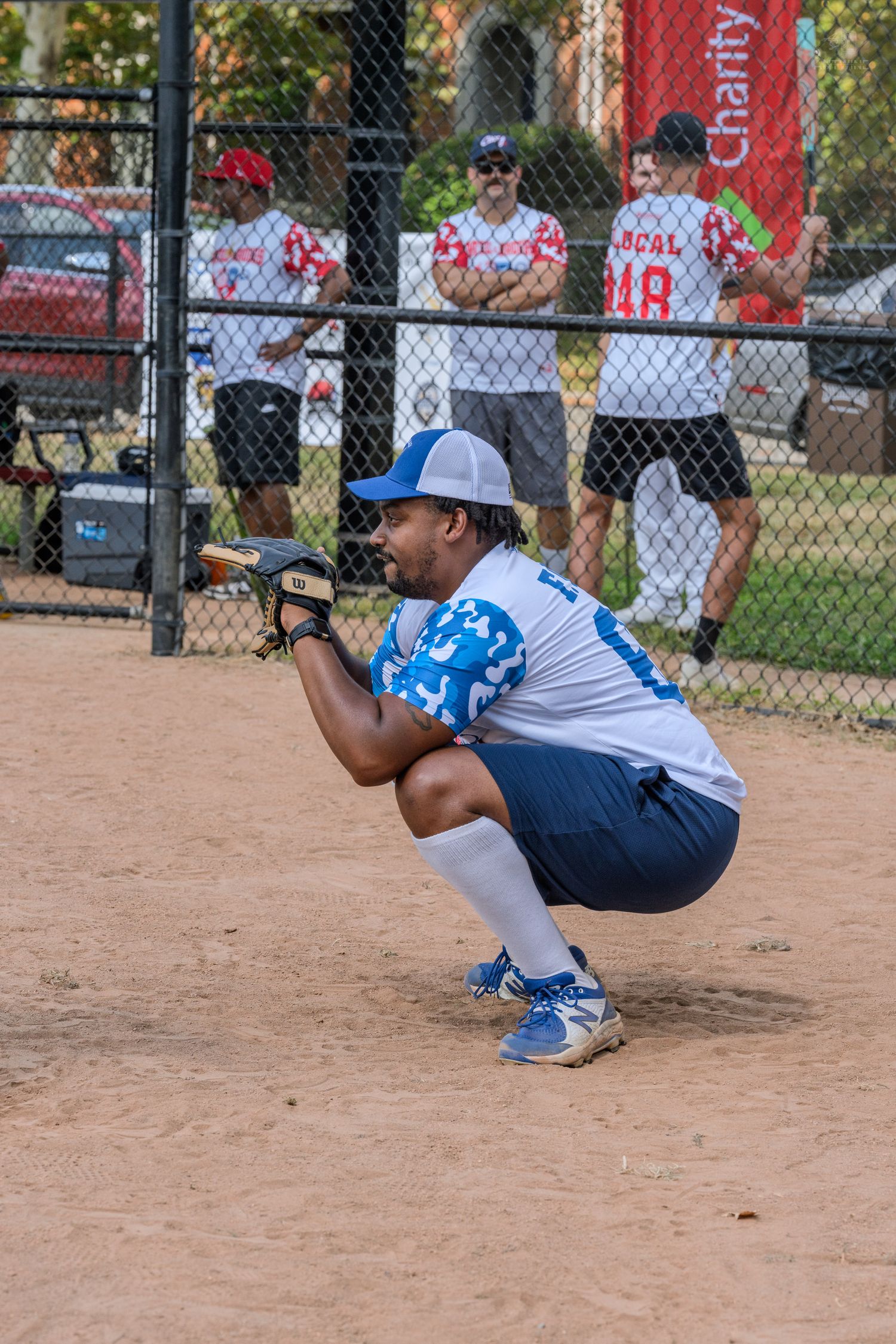 Softball catcher in blue and white uniform crouching in ready position during a charity game.