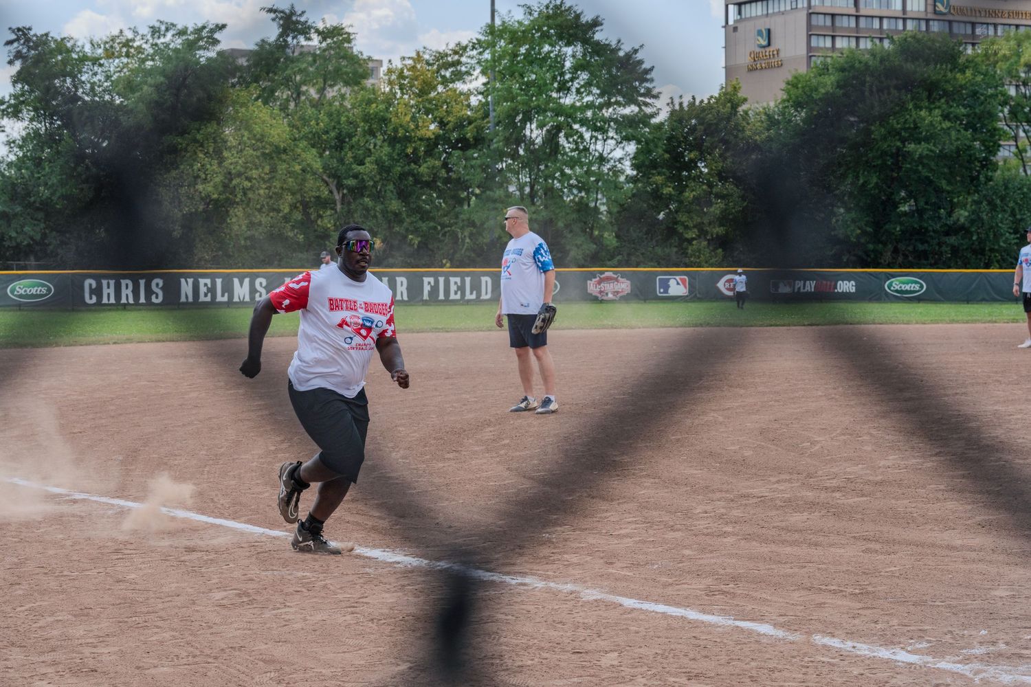 Softball player running the bases at Chris Nelms Field during an outdoor game on a sunny day.