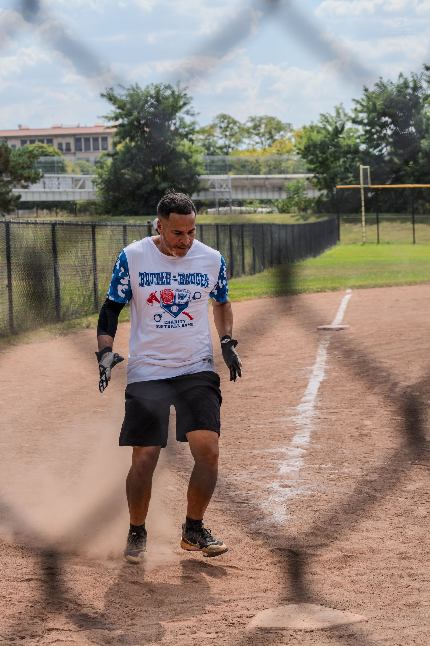 A softball player runs the bases on a sunny day wearing a Battle of Badges tournament jersey.