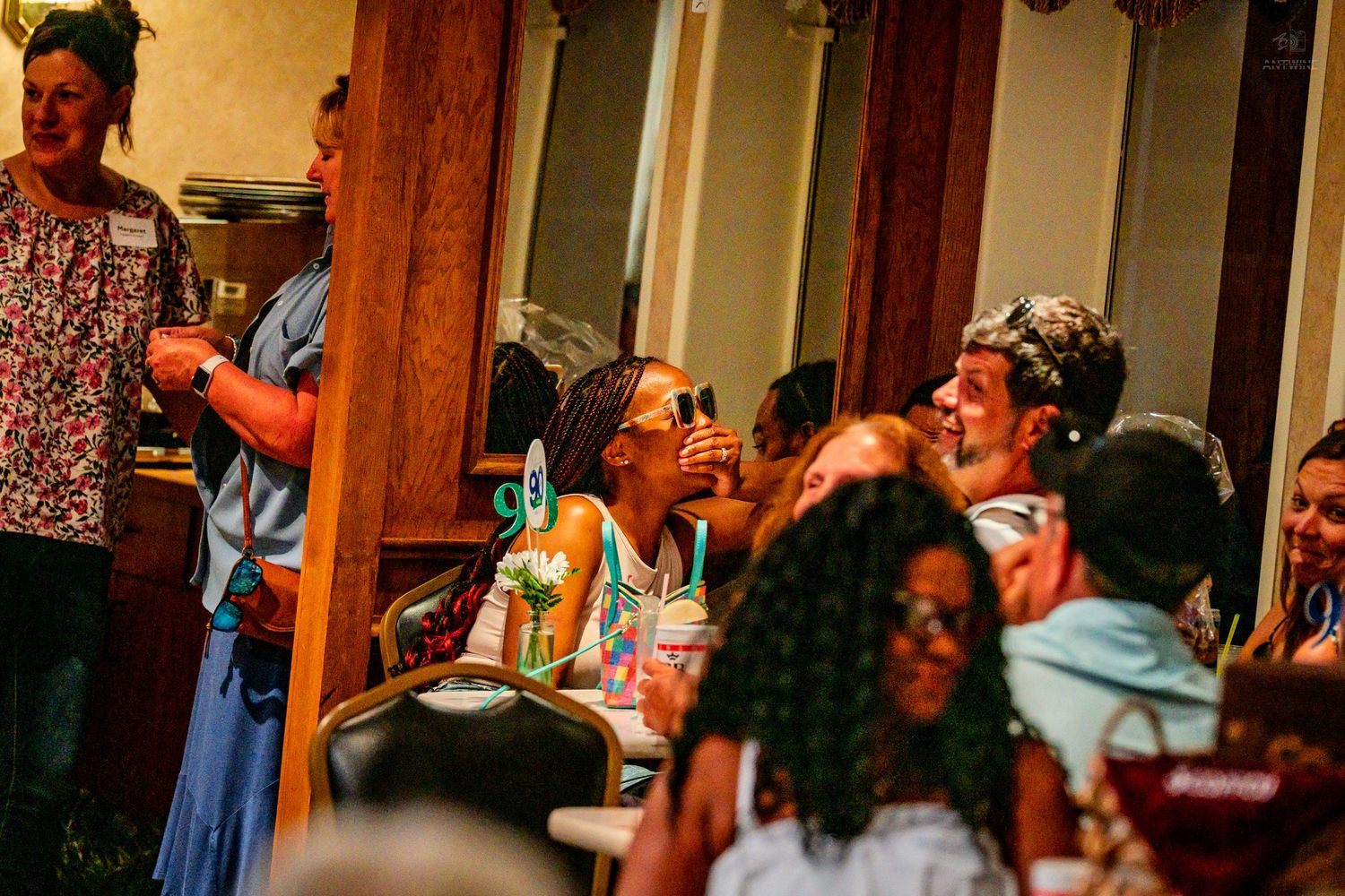 Diverse group of women laughing and enjoying drinks at a lively indoor social event.