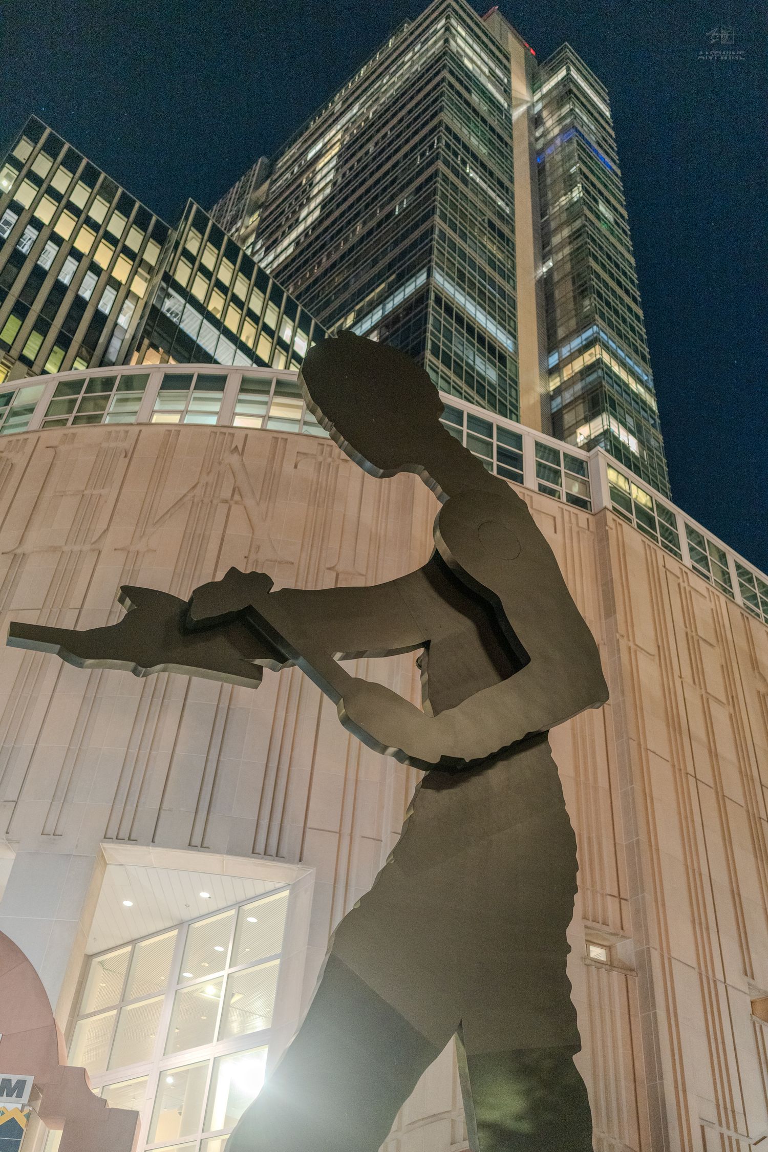 Large bronze Hammering Man sculpture silhouetted against illuminated skyscrapers at night in Seattle.