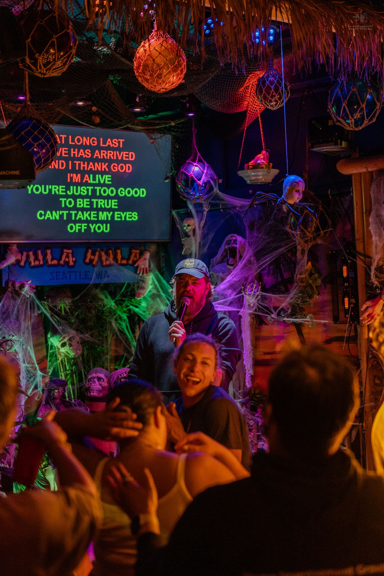 Lively Halloween karaoke night at Hula Hula bar with colorful neon lights and spooky decorations.