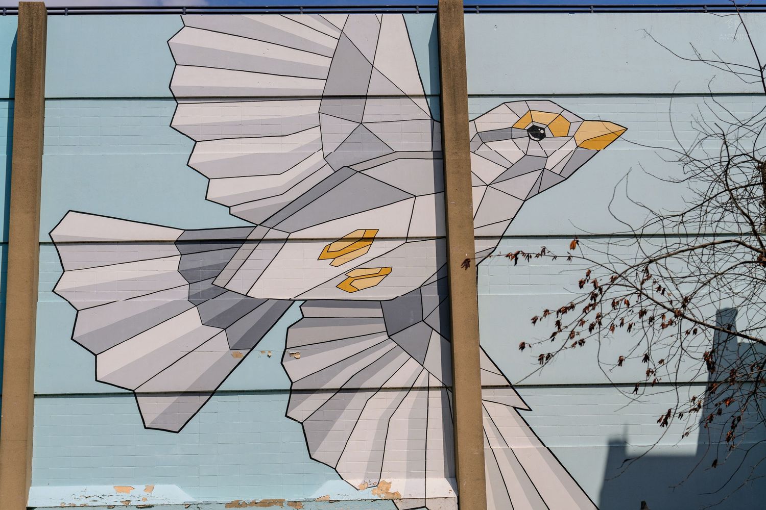 Geometric mosaic mural of a white bird in flight on a building wall.