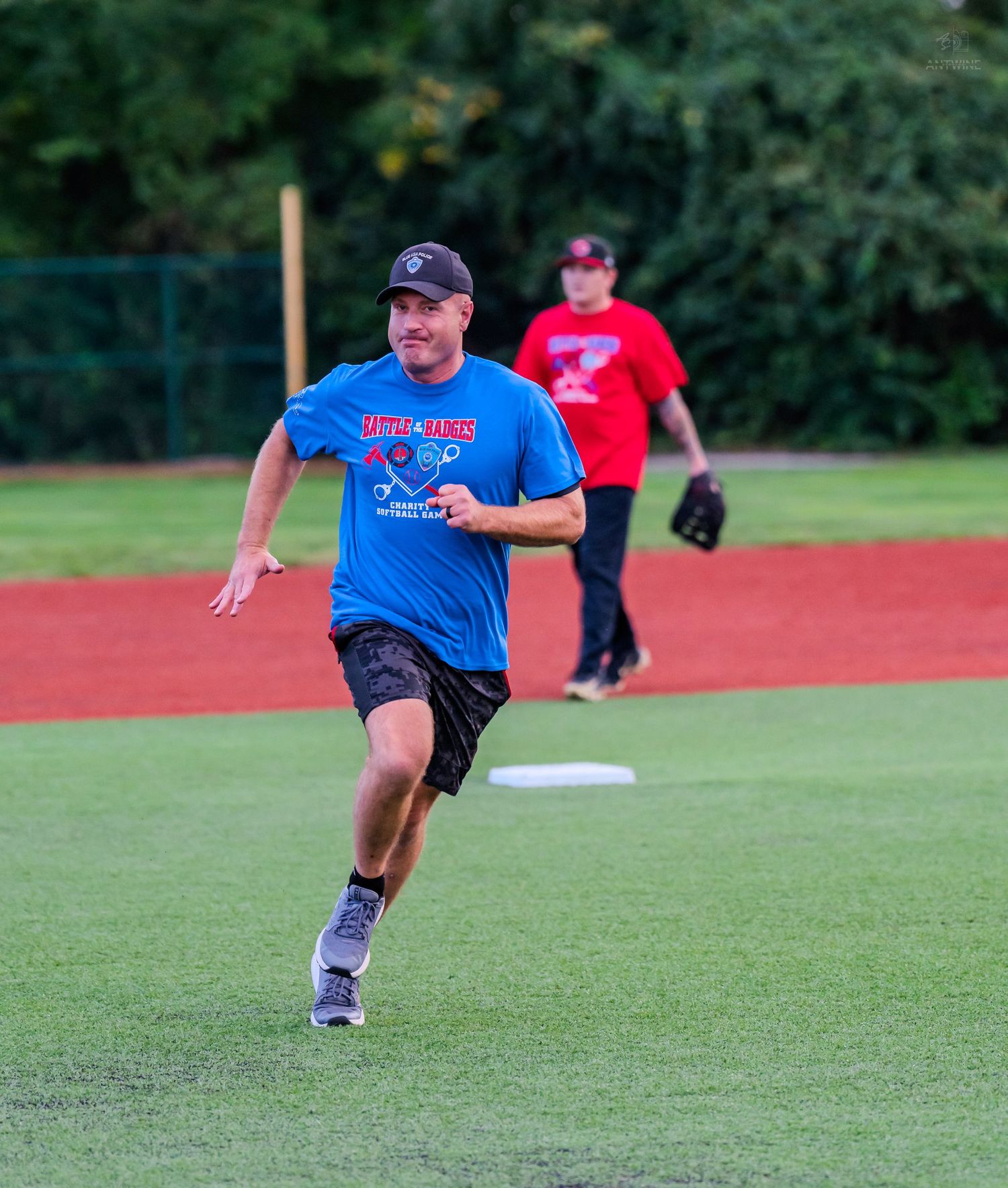 Man in blue softball jersey runs bases during a recreational baseball game on a green field.