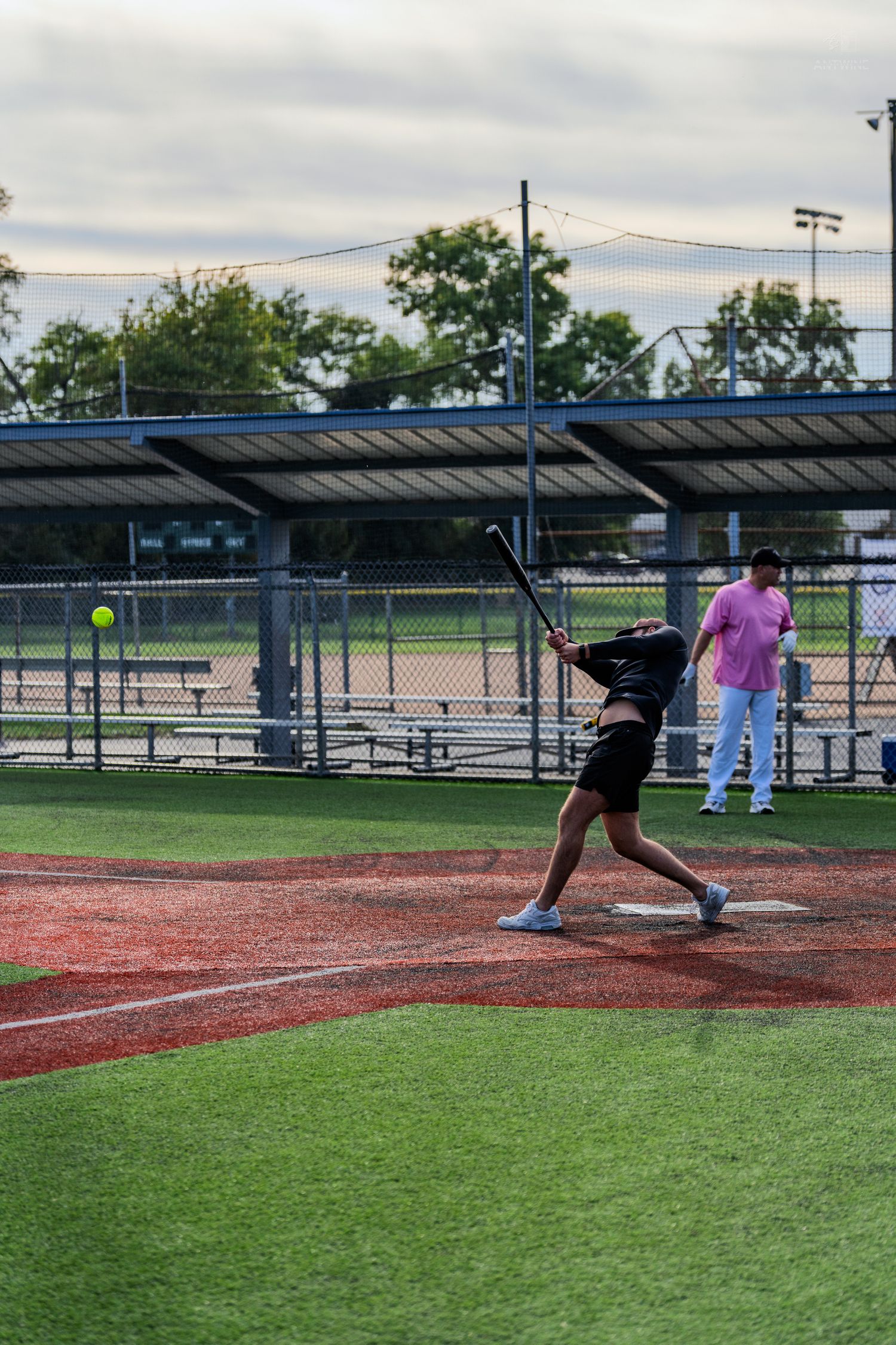 Batter swinging at a softball during a recreational game on a well-maintained diamond field with dugout in background.
